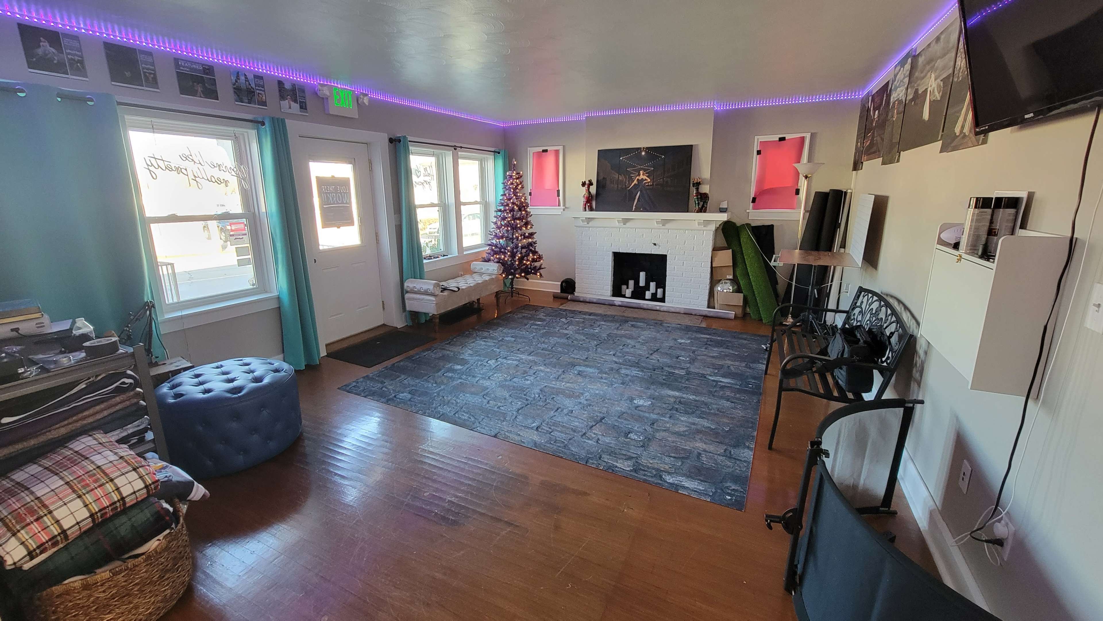 A spacious room with a hardwood floor, decorated with a Christmas tree, a large decorative rug, and various seating and storage areas.