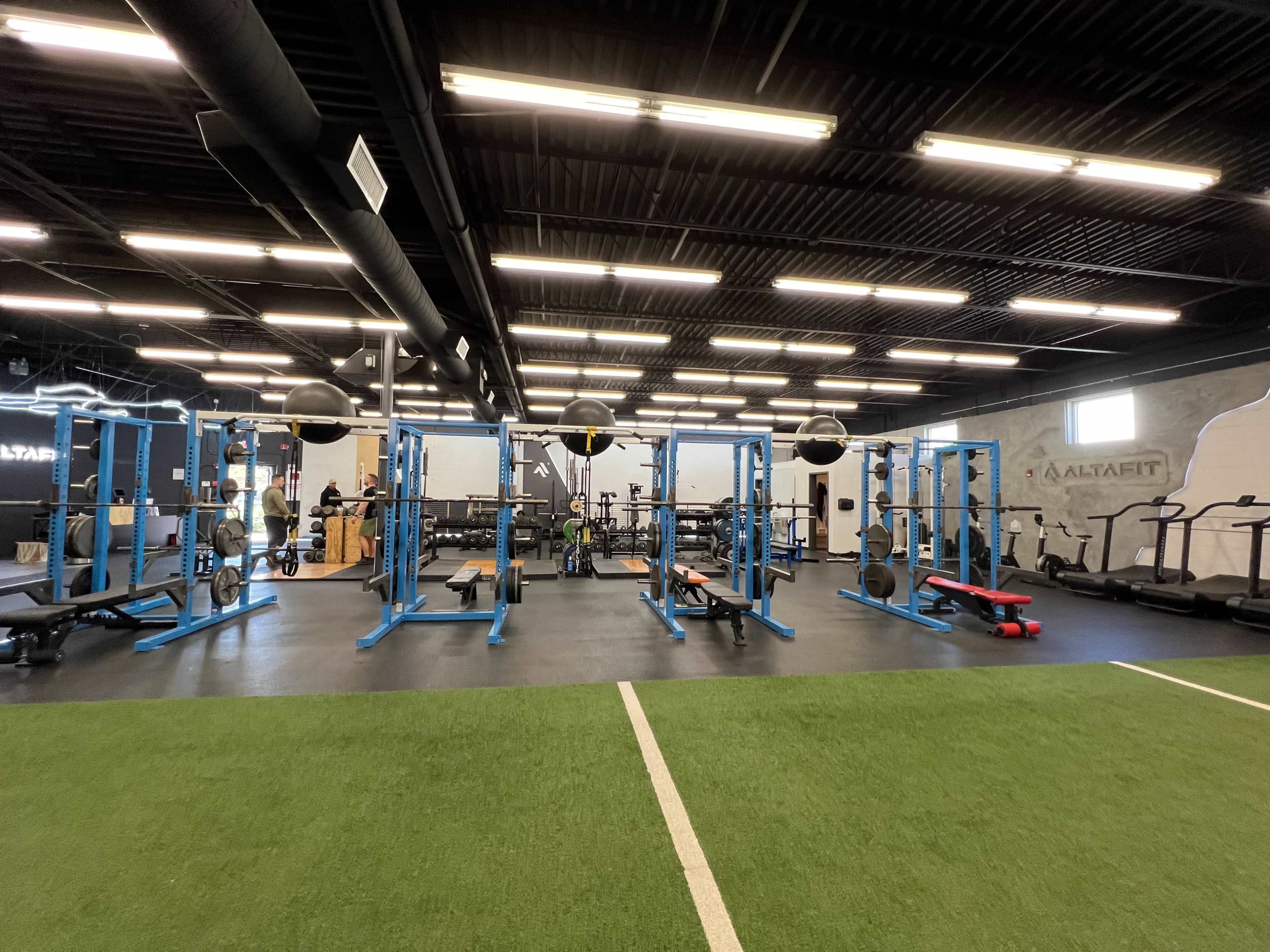 A gym interior featuring blue weightlifting equipment, treadmills, and a turf area.