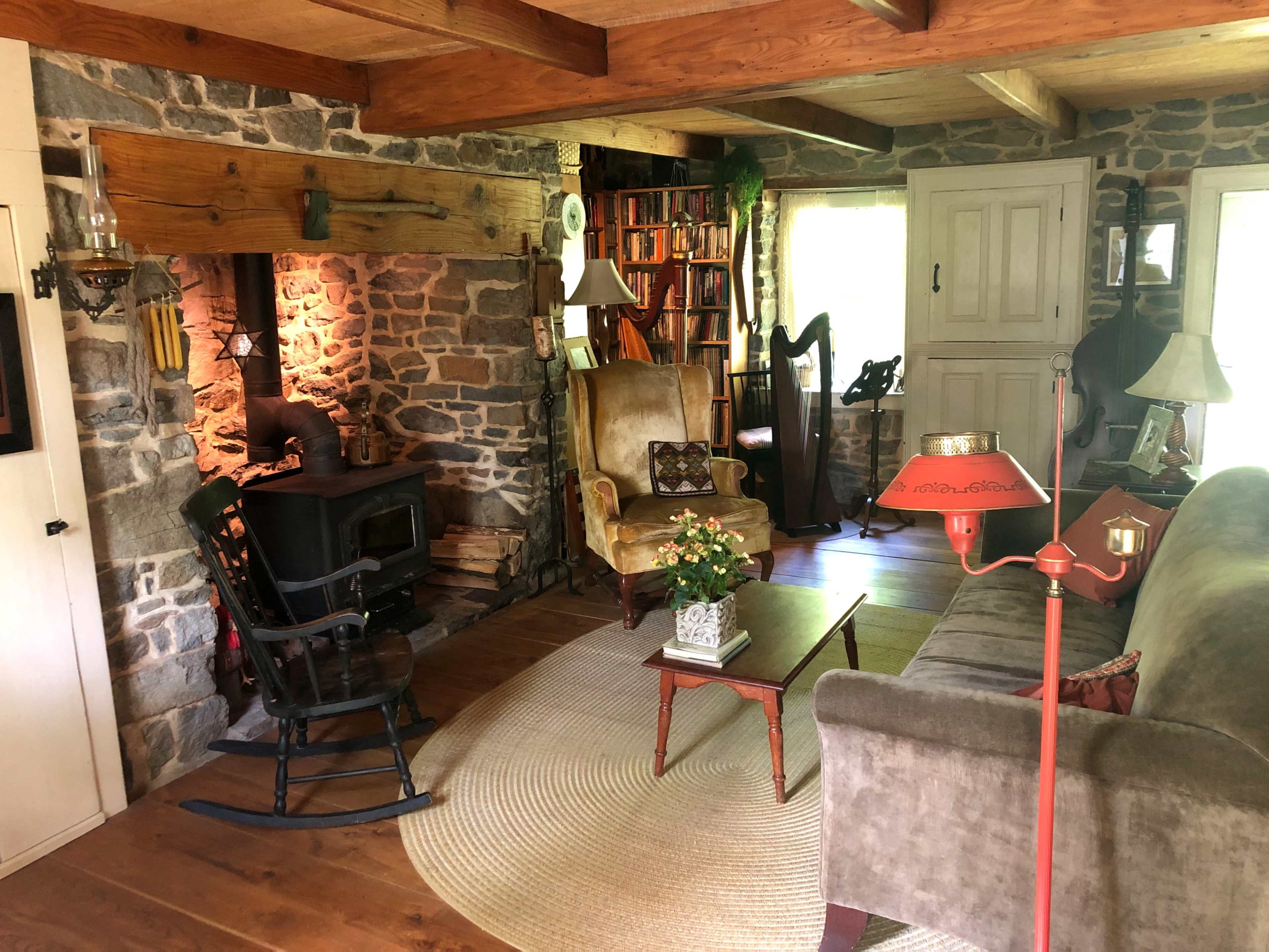 The image shows a cozy living room featuring a stone fireplace, a comfortable sofa, a rocking chair, and various wooden furniture pieces.