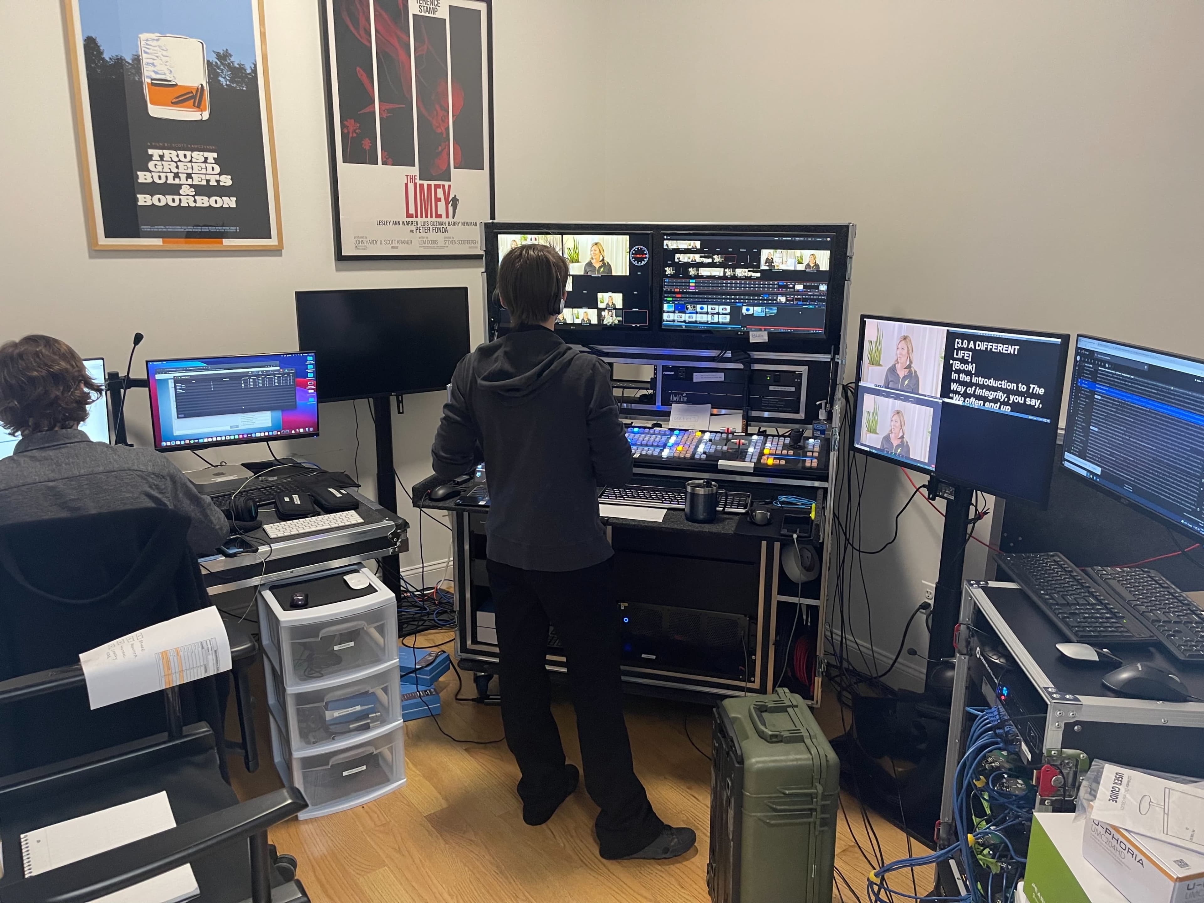 A person operates a video production setup with multiple monitors and equipment in a room featuring film posters on the walls.