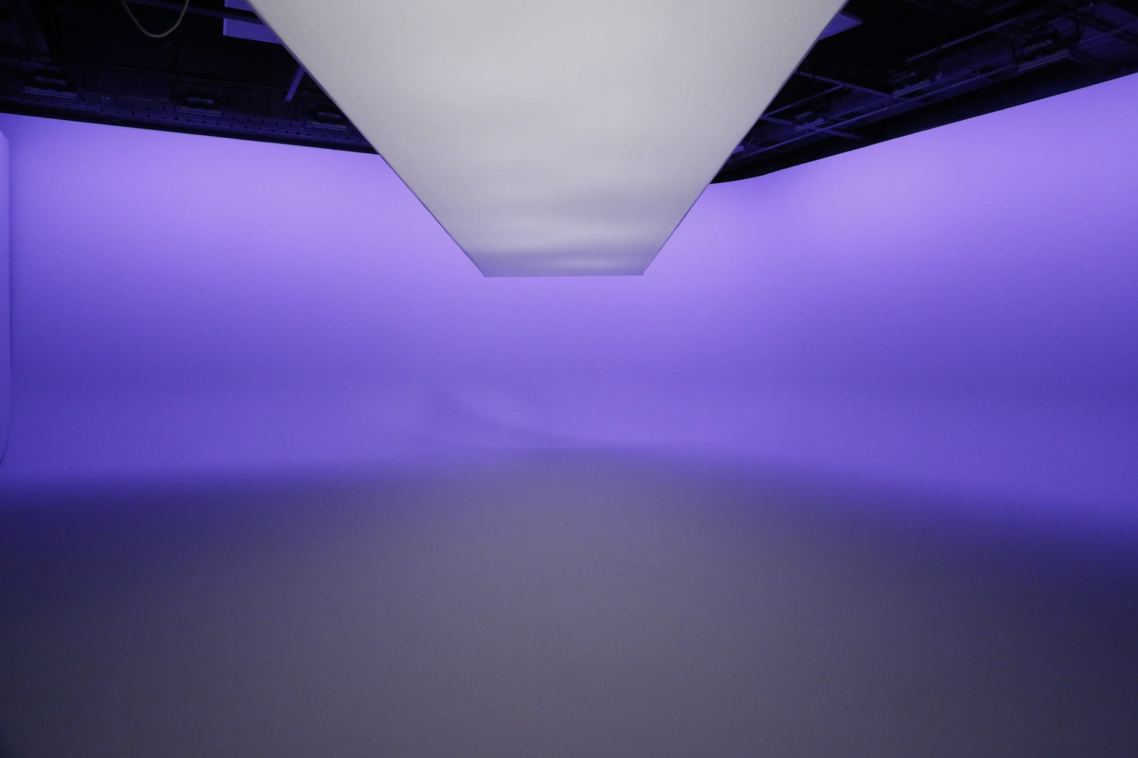 A studio space with a large, flat light source hanging above and a purple gradient background.