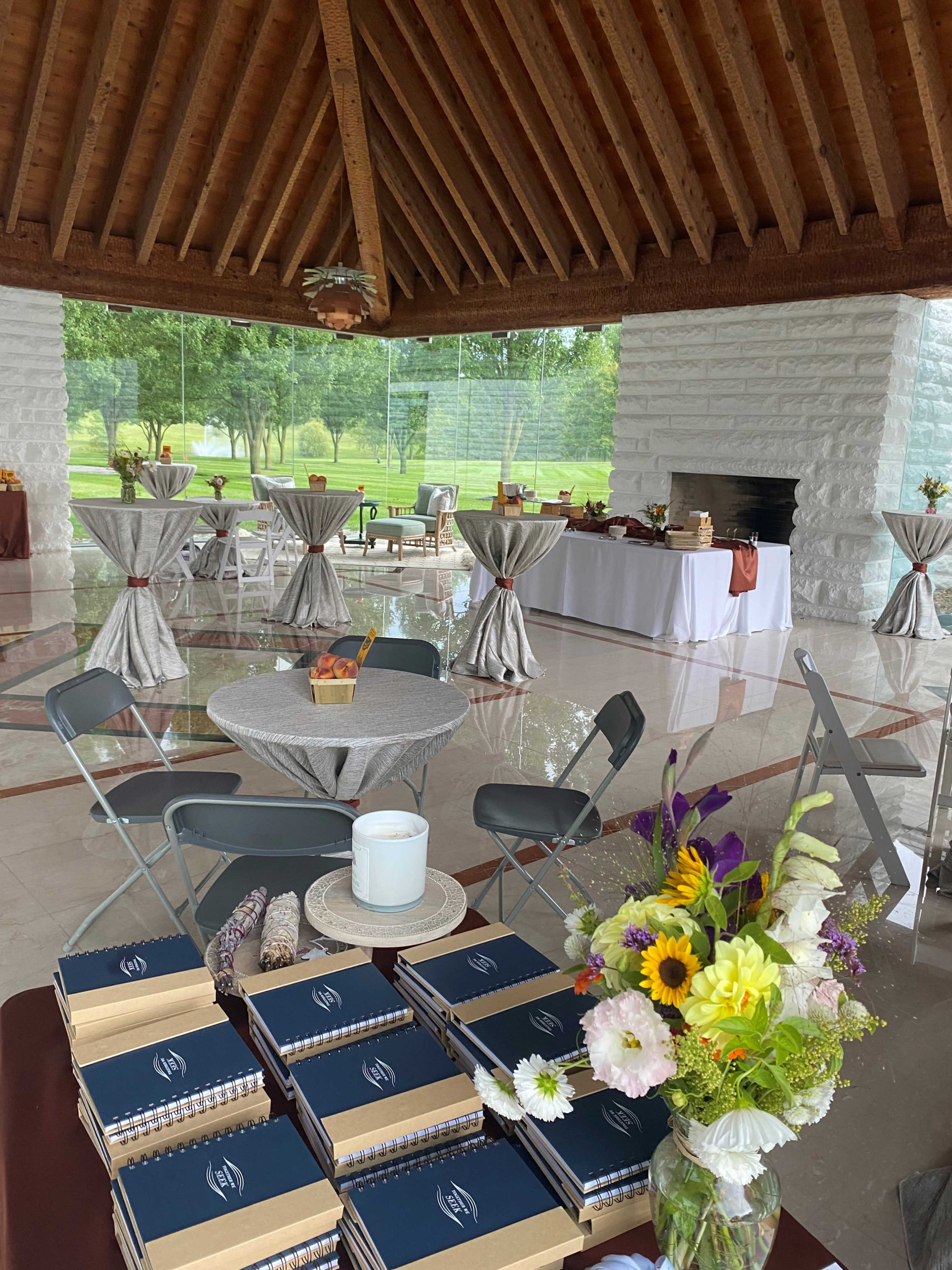 The photo shows an elegantly arranged indoor event space with tables dressed in gray, a buffet table, and floral centerpieces.