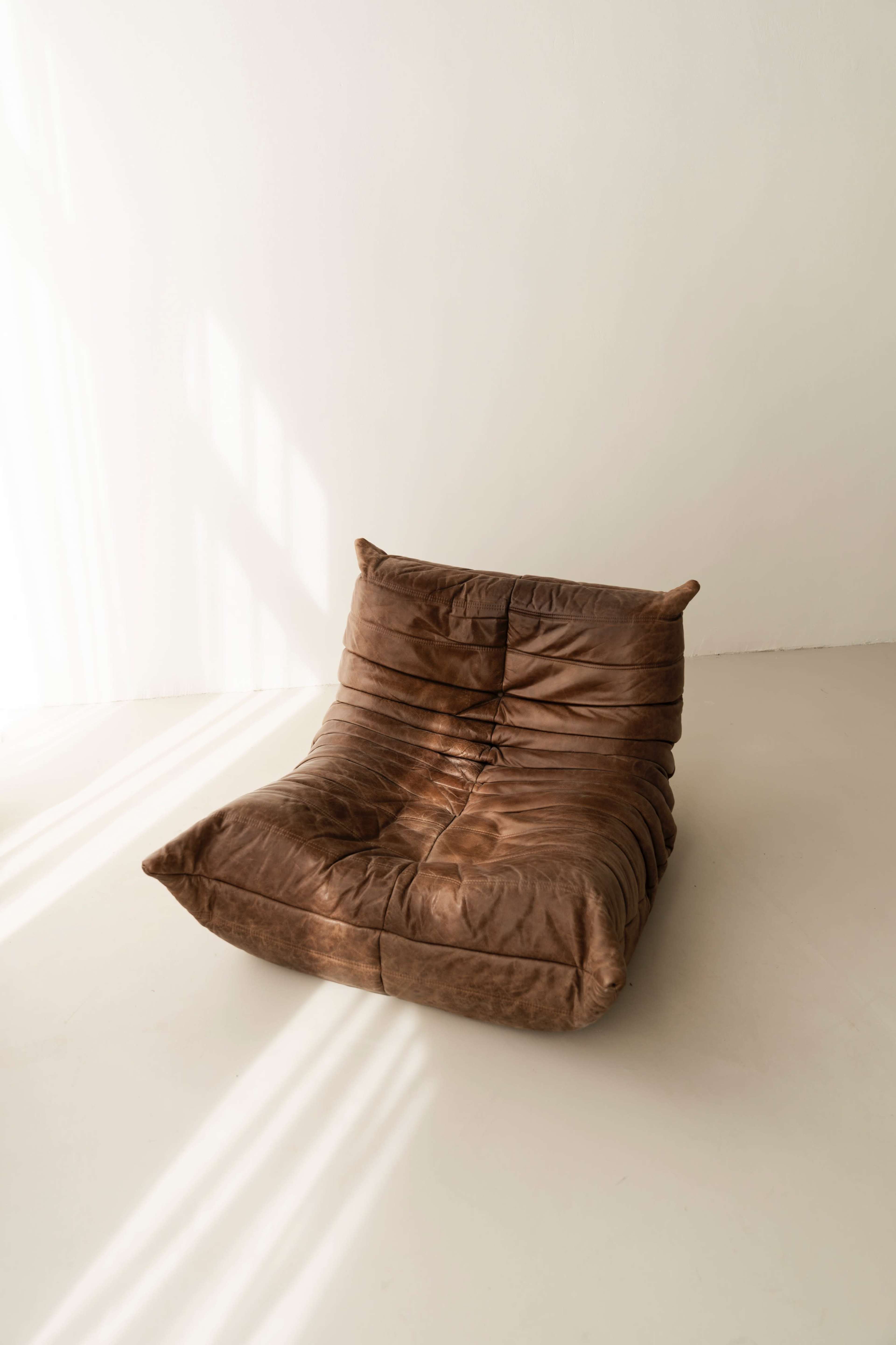 A brown, plush chair is positioned on a light-colored floor, illuminated by soft natural light streaming through a nearby window.