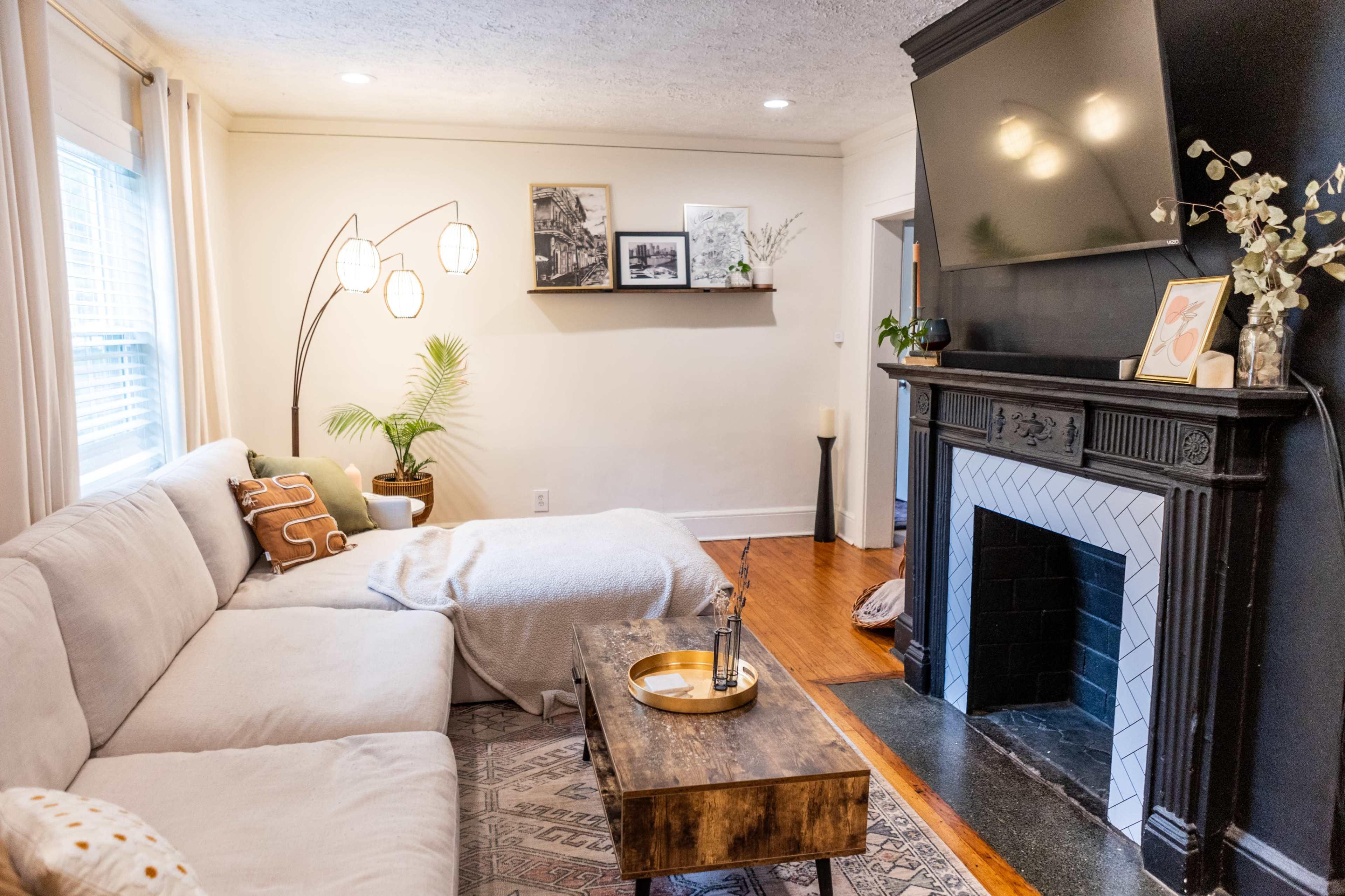 A living room features a light-colored sectional sofa, a wooden coffee table, and a fireplace with a television mounted above it.