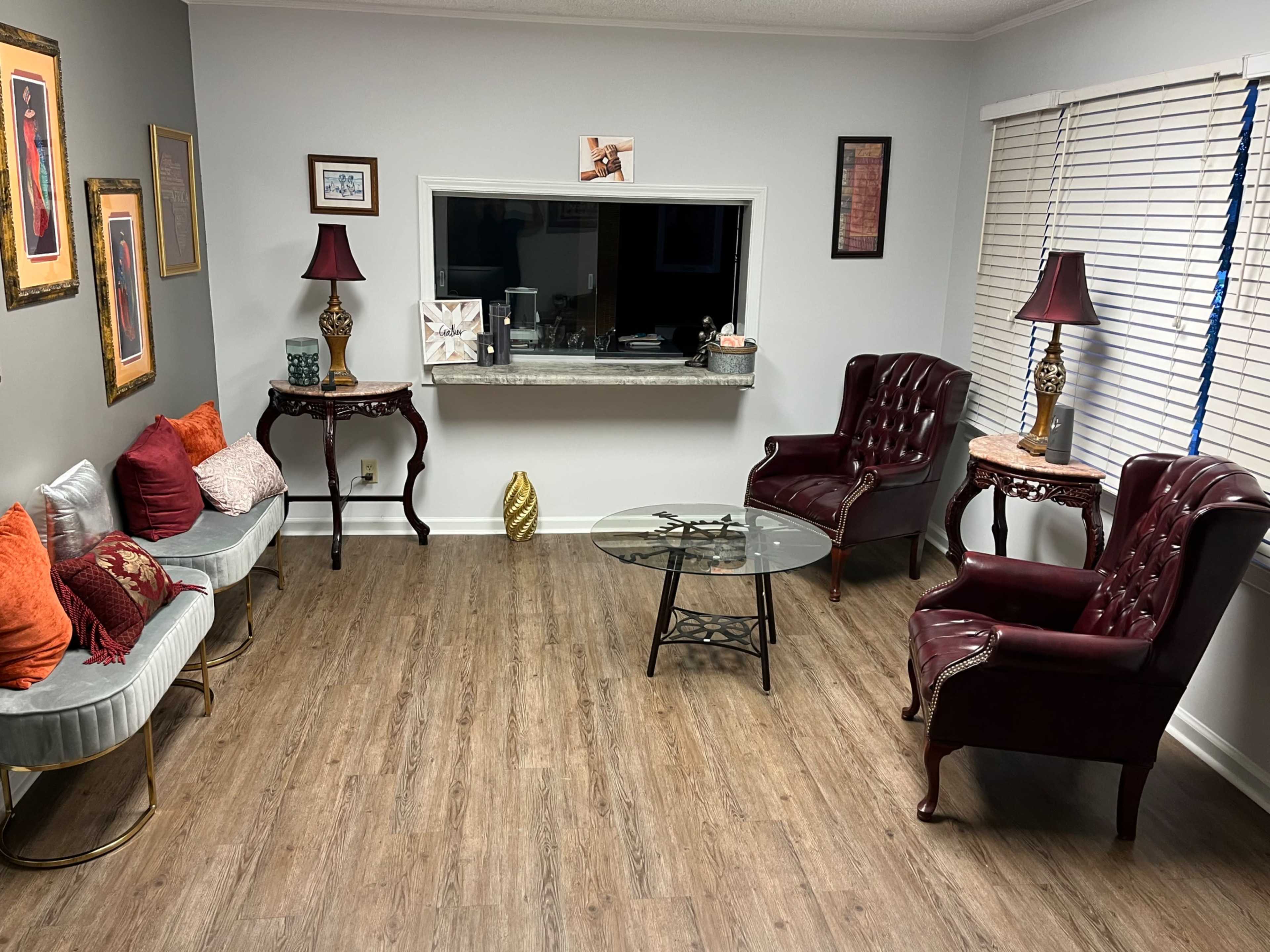 The image shows a cozy living room with two burgundy armchairs, a glass coffee table, and decorative artwork on the walls.