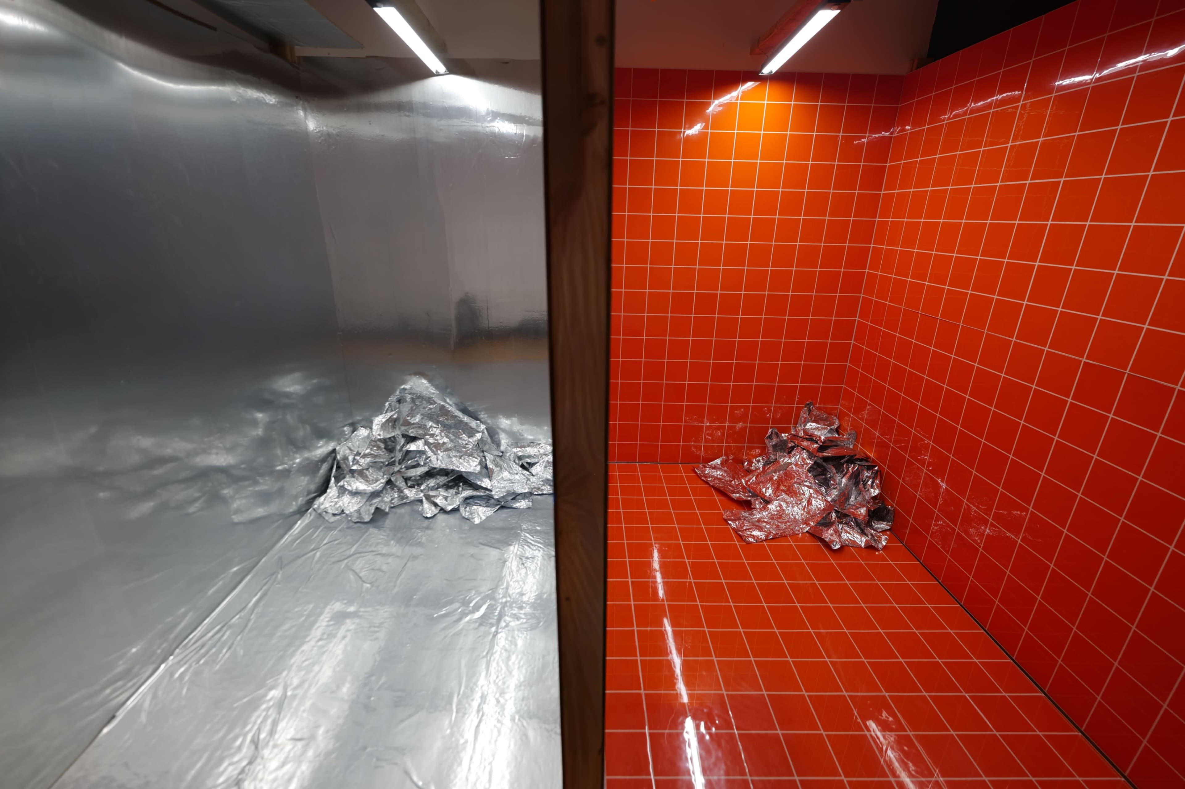 The image shows a divided room, half lined with shiny silver foil and the other half with bright red tiles, each containing a pile of crumpled silver material.