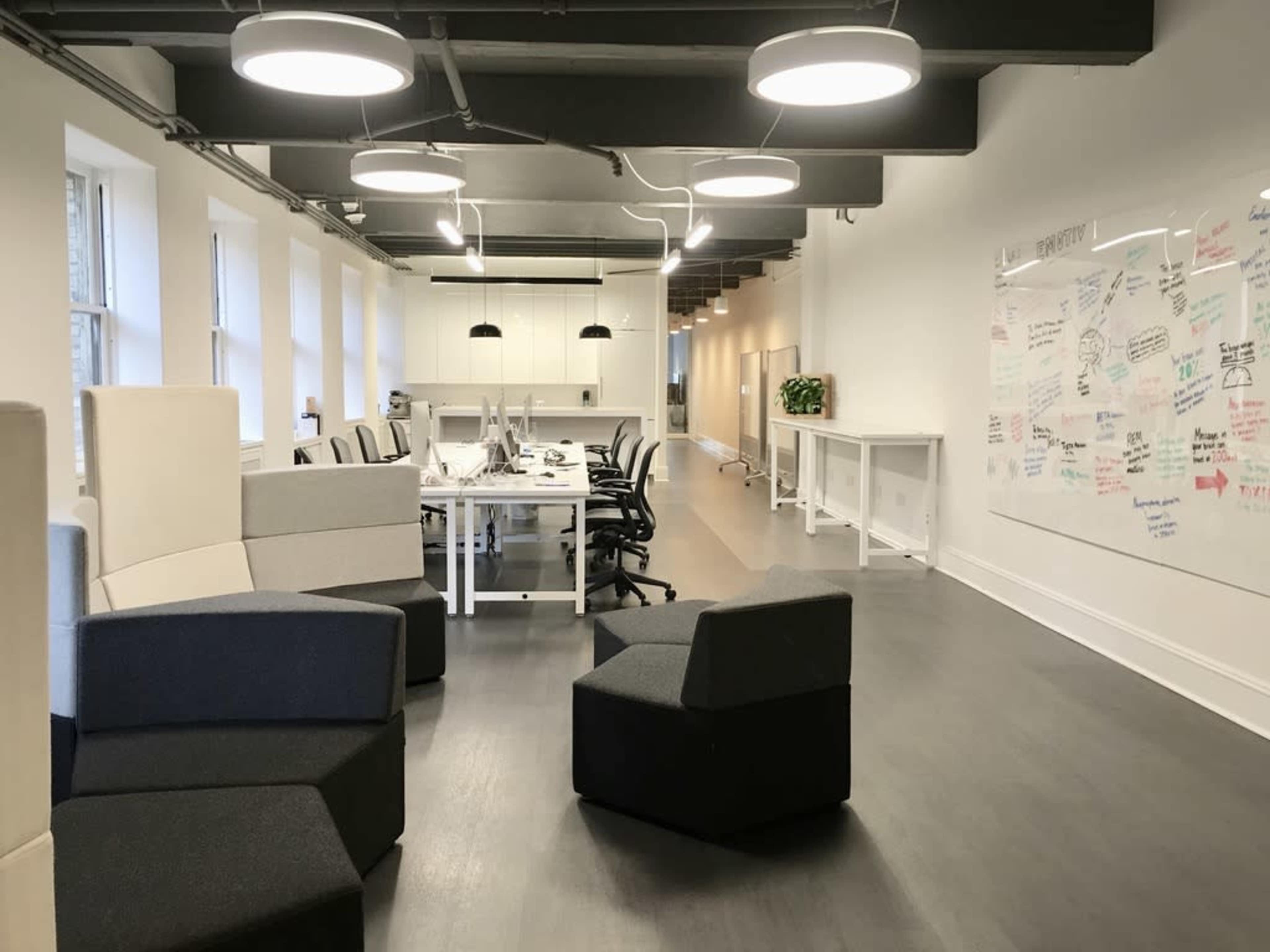A modern office space with a row of desks and a whiteboard covered in notes, surrounded by distinctive seating arrangements.
