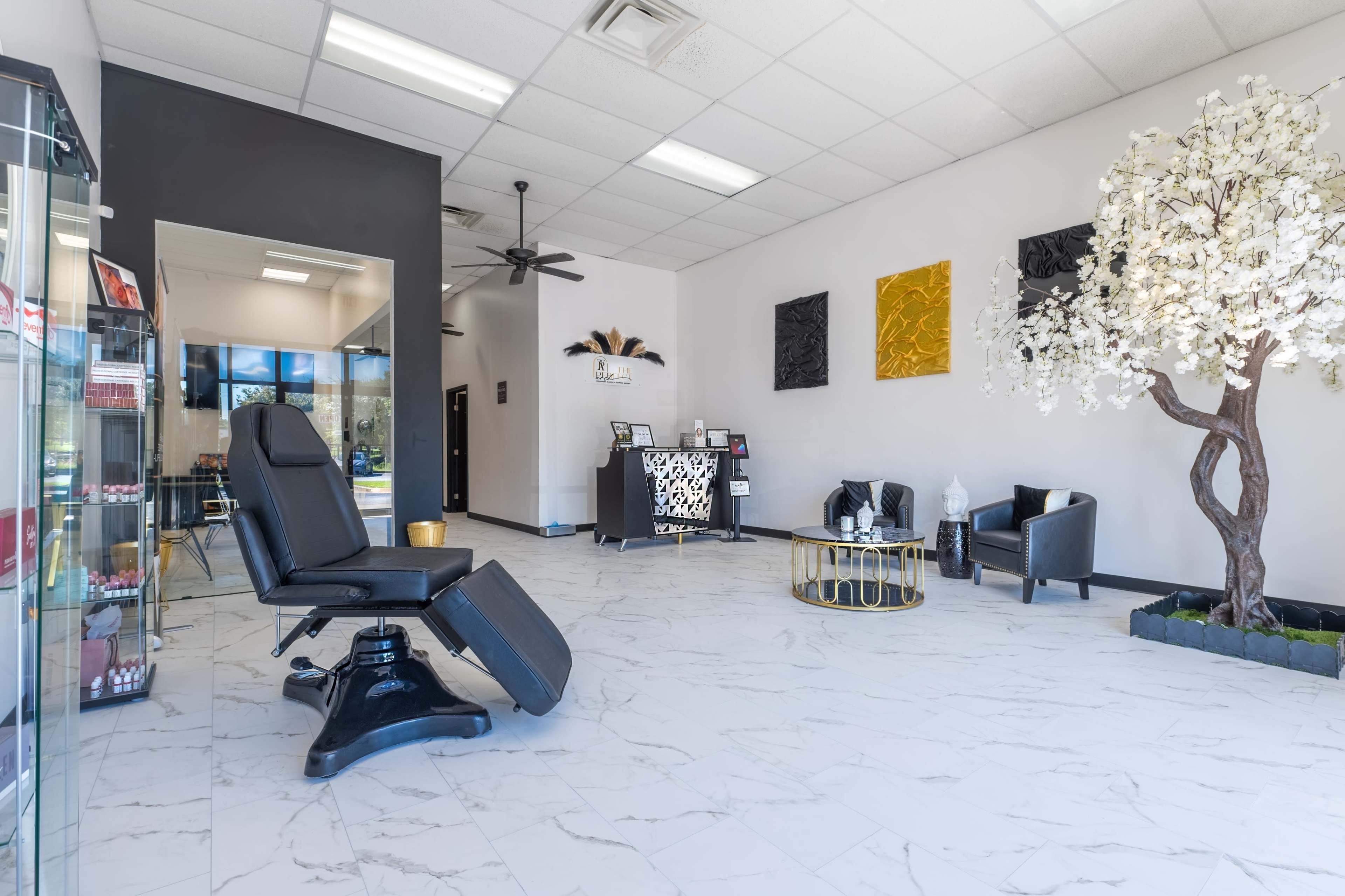 A spacious, modern interior of a salon featuring a reclining chair, a reception desk, and decorative elements including a potted tree and wall art.