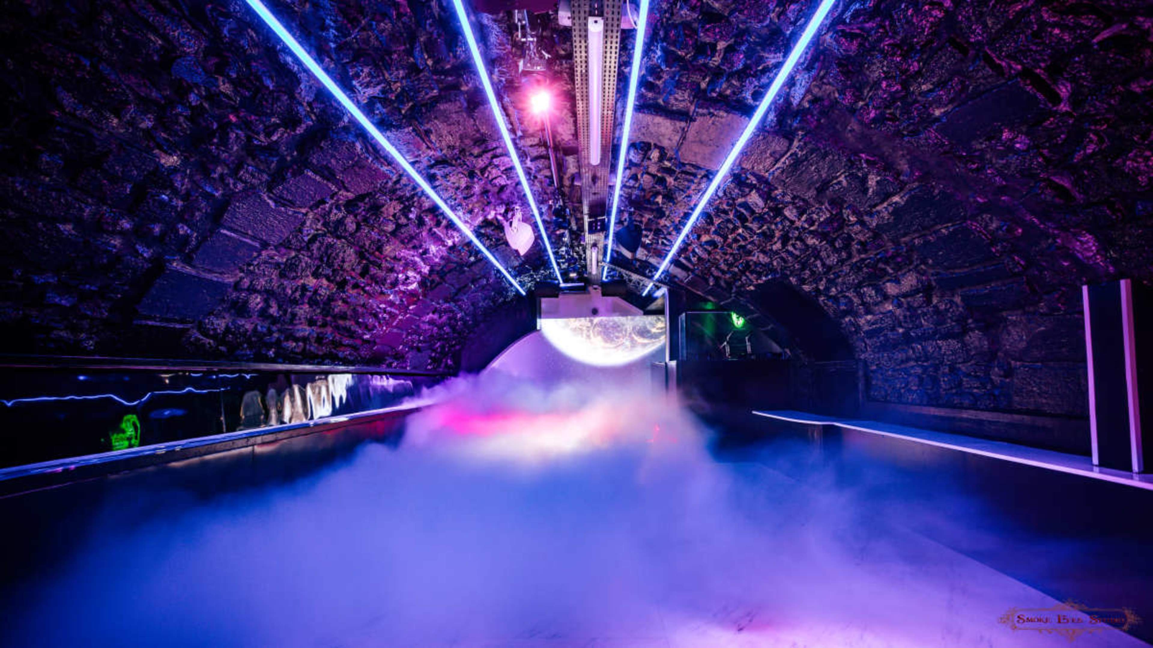 A dimly lit tunnel featuring colorful neon lights and a layer of fog covering the ground.
