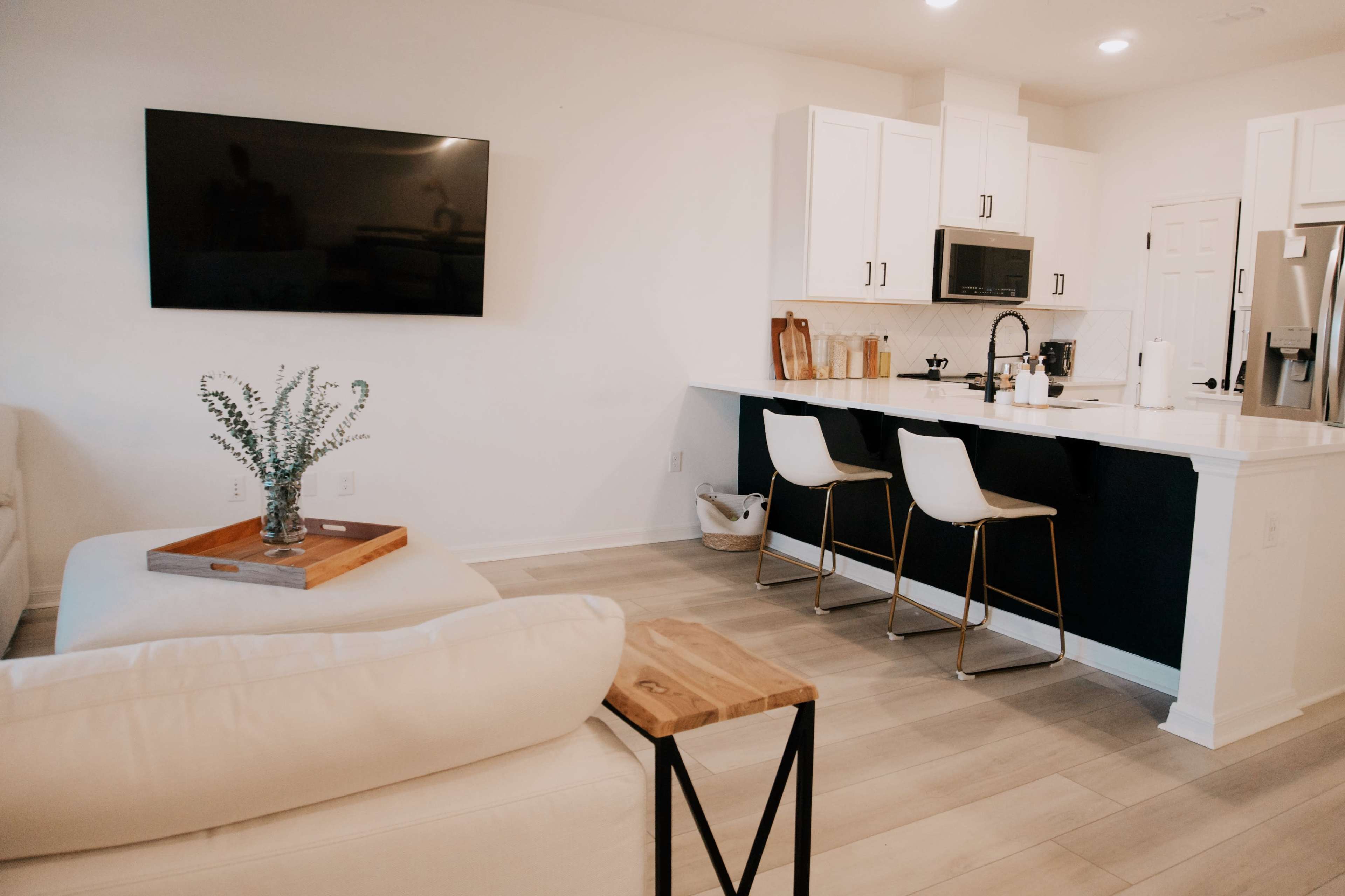 A modern kitchen and living area with a white sofa, a wooden side table, and a kitchen counter with bar stools.