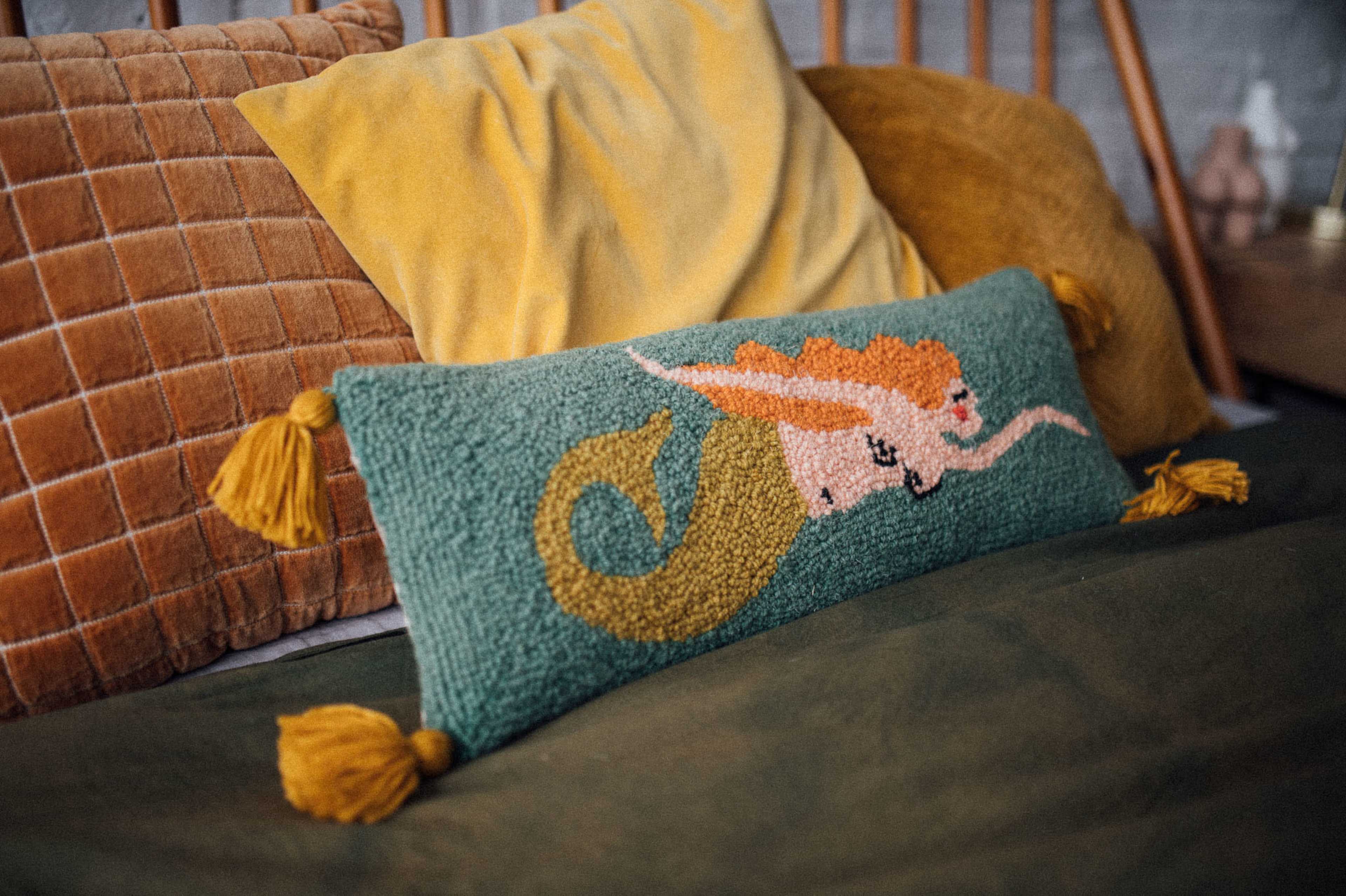 A colorful decorative pillow featuring a whimsical design sits on a bed with textured cushions and a green blanket.