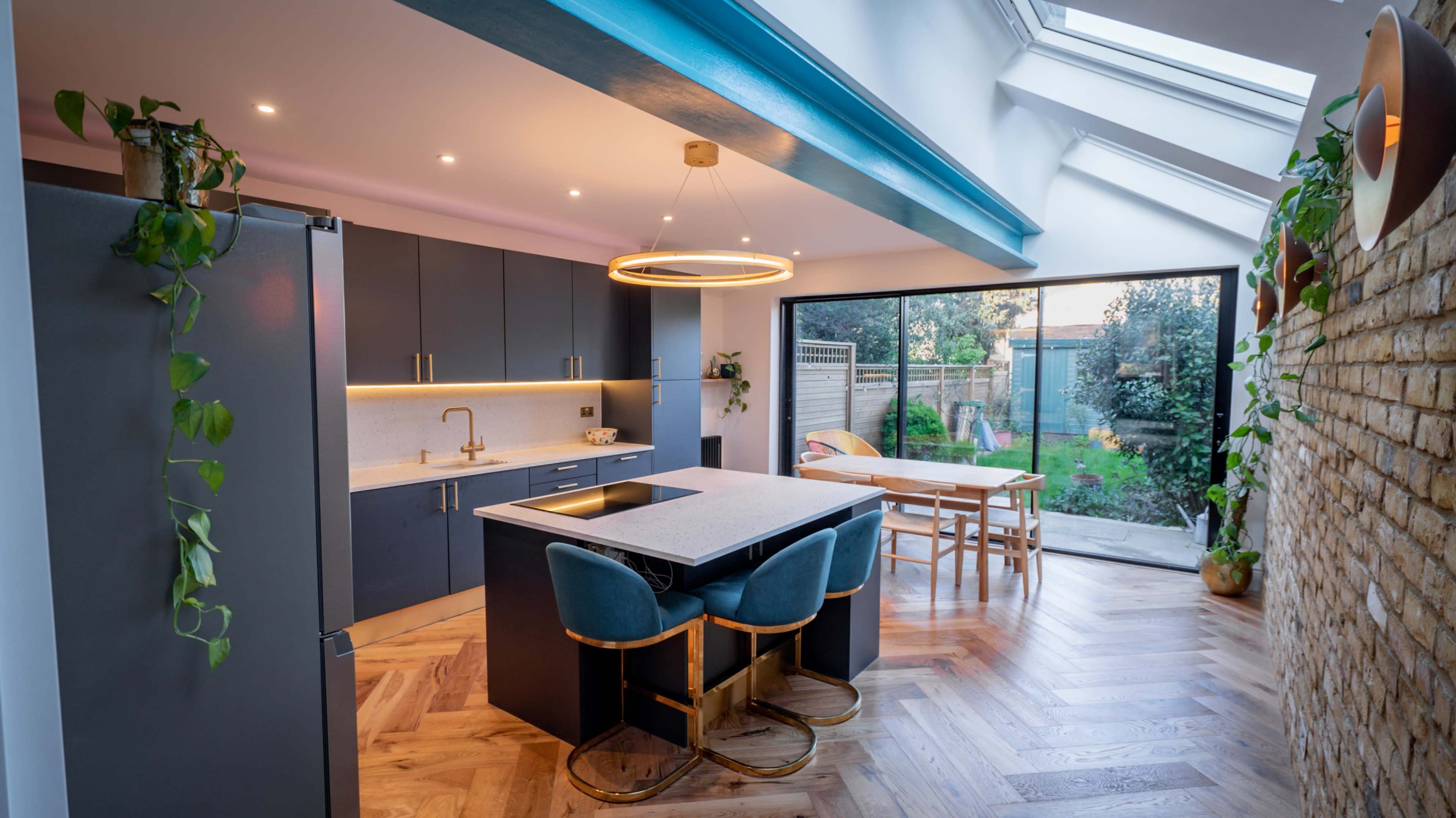 A modern kitchen features gray cabinetry, a central island with a sink, and large glass doors opening to a garden.