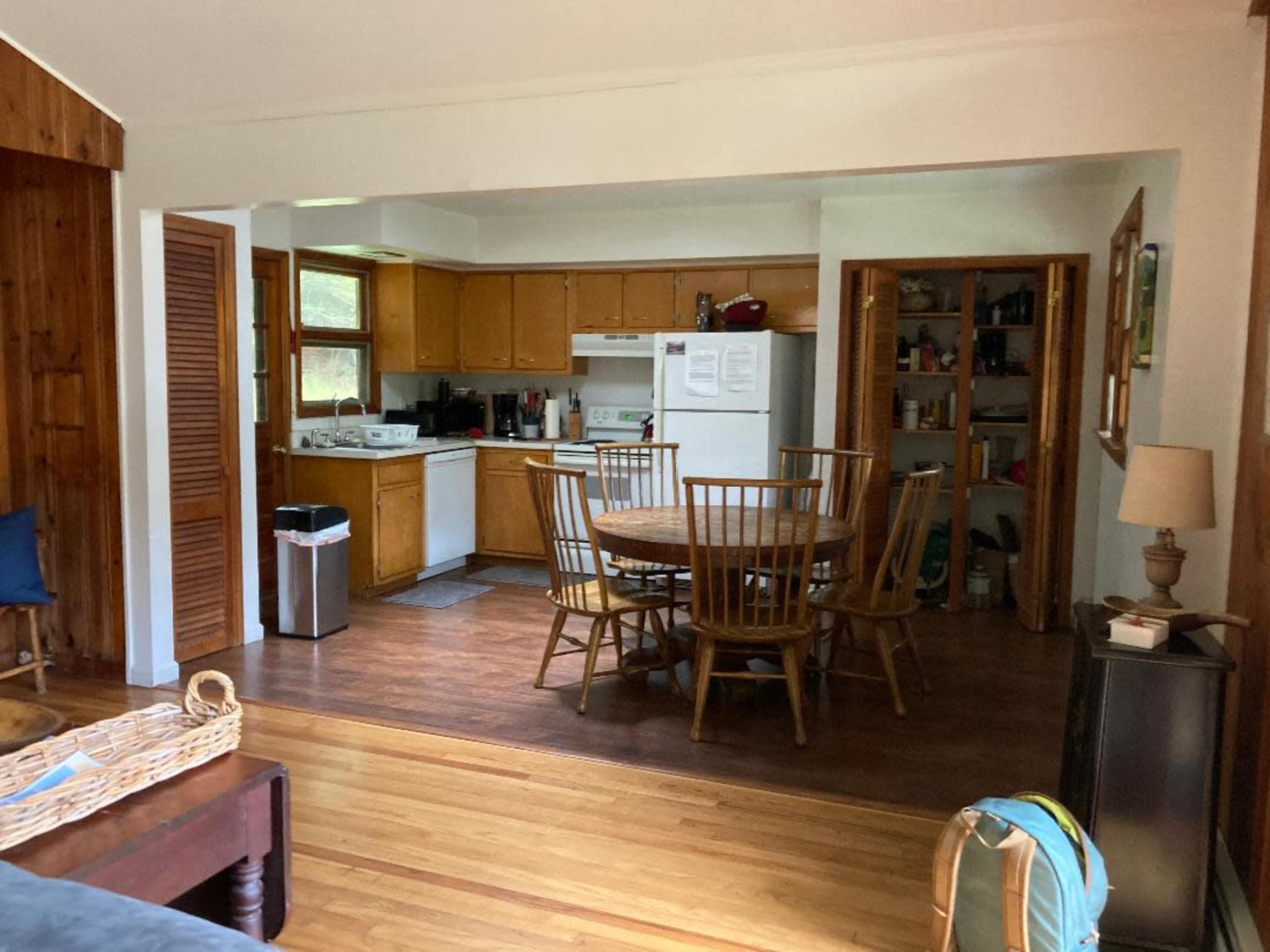 A kitchen and dining area with wooden cabinets, a round table surrounded by chairs, and a visible refrigerator and pantry.