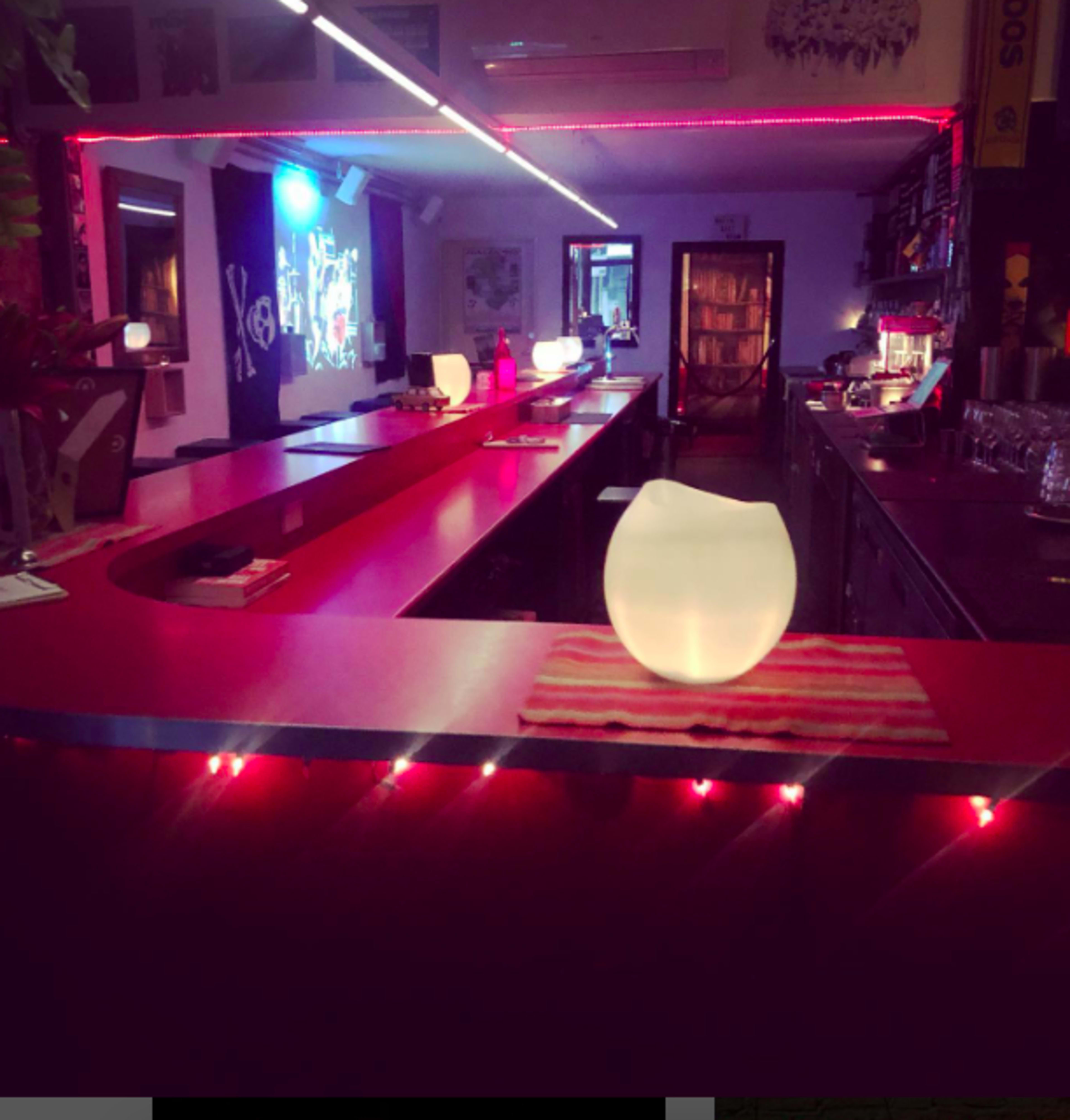 A brightly lit bar features a red counter with illuminated decor and vibrant colors reflecting off the walls.
