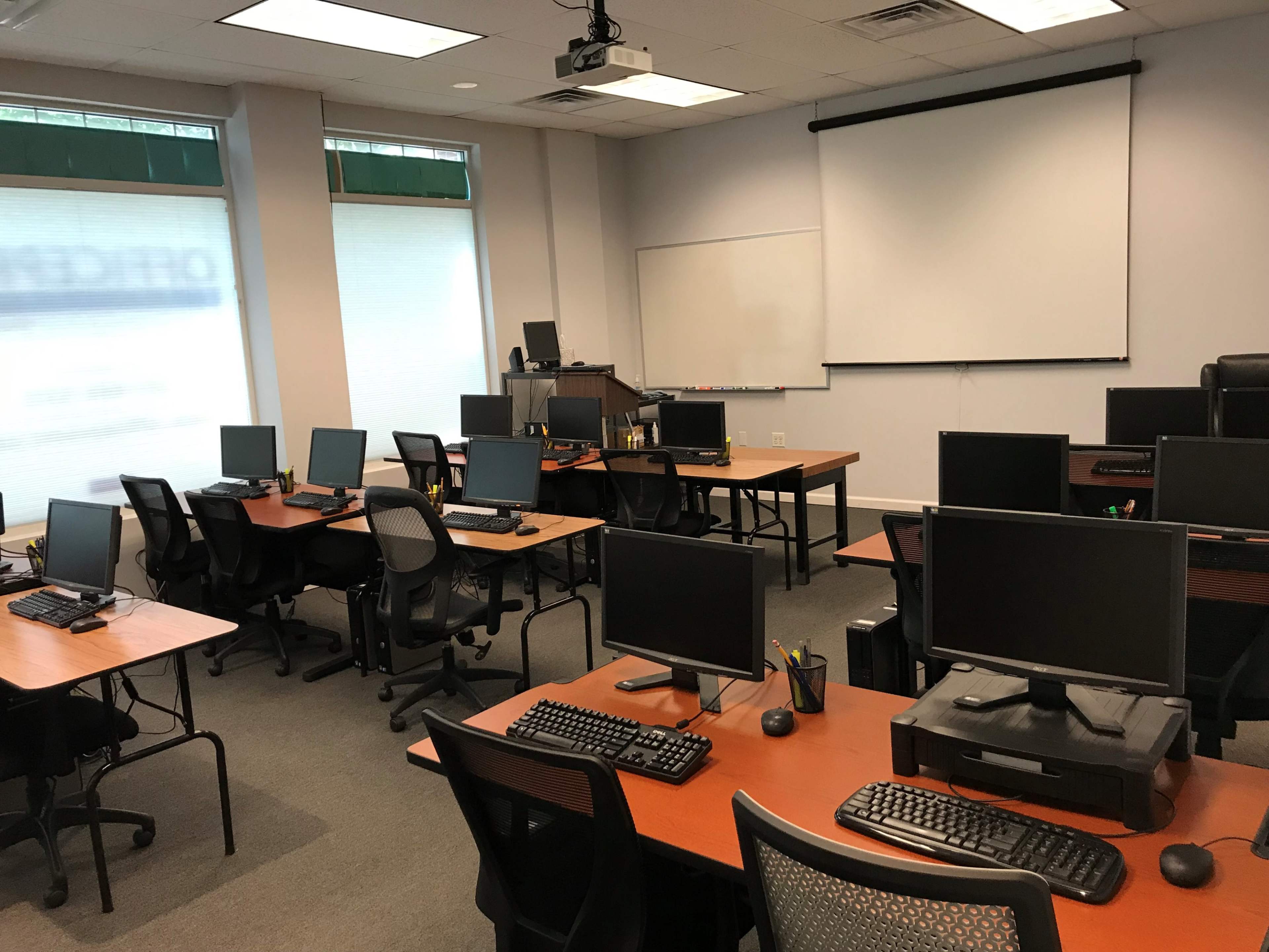 A computer lab with multiple desks equipped with desktop computers and chairs arranged in a spacious room.