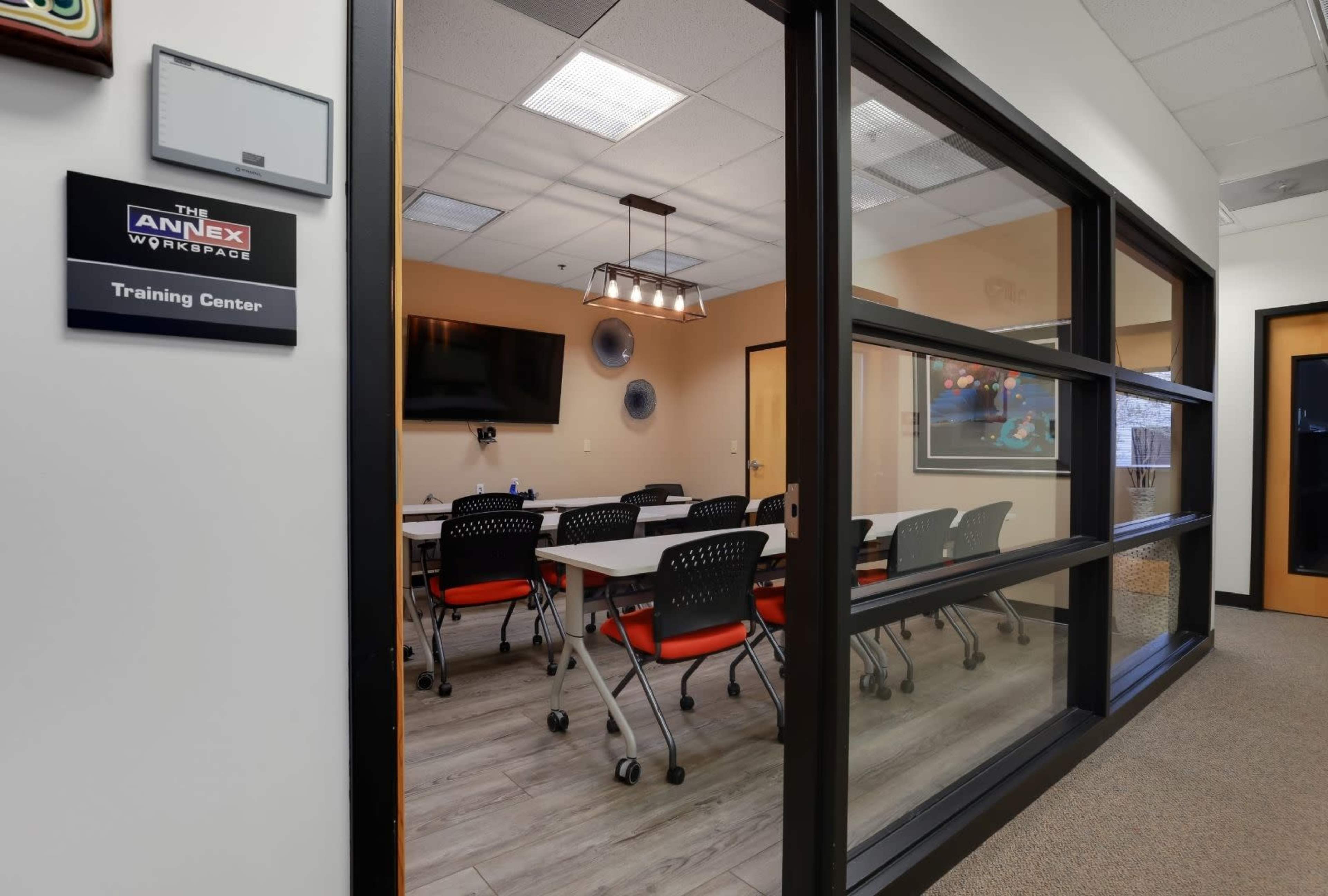 A training center with rows of tables and chairs is visible through a glass wall, featuring a television and wall decorations.