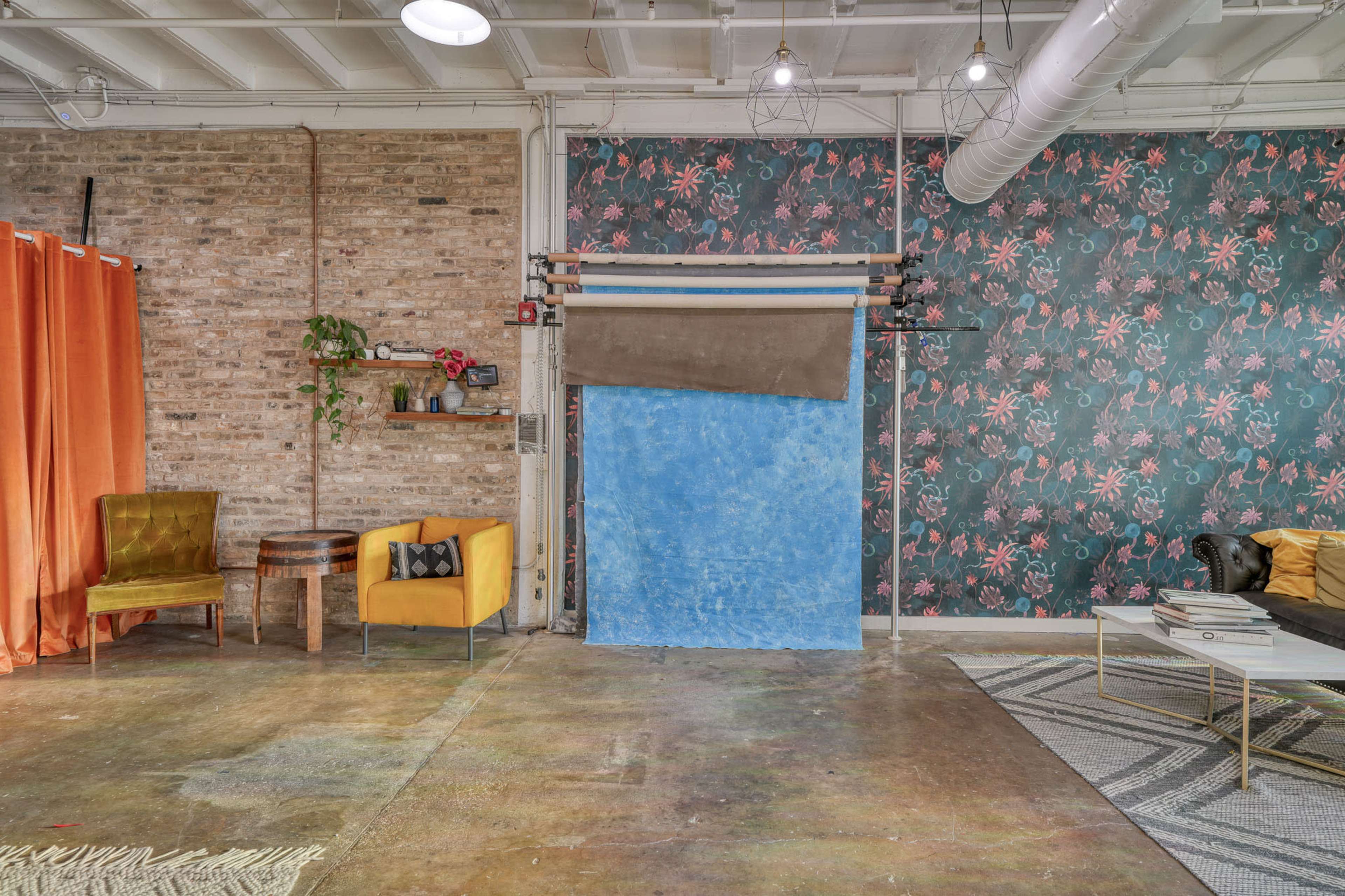 The image shows a styled studio space featuring a colorful patterned wall, a blue backdrop, a mix of seating options, and a variety of decor elements.