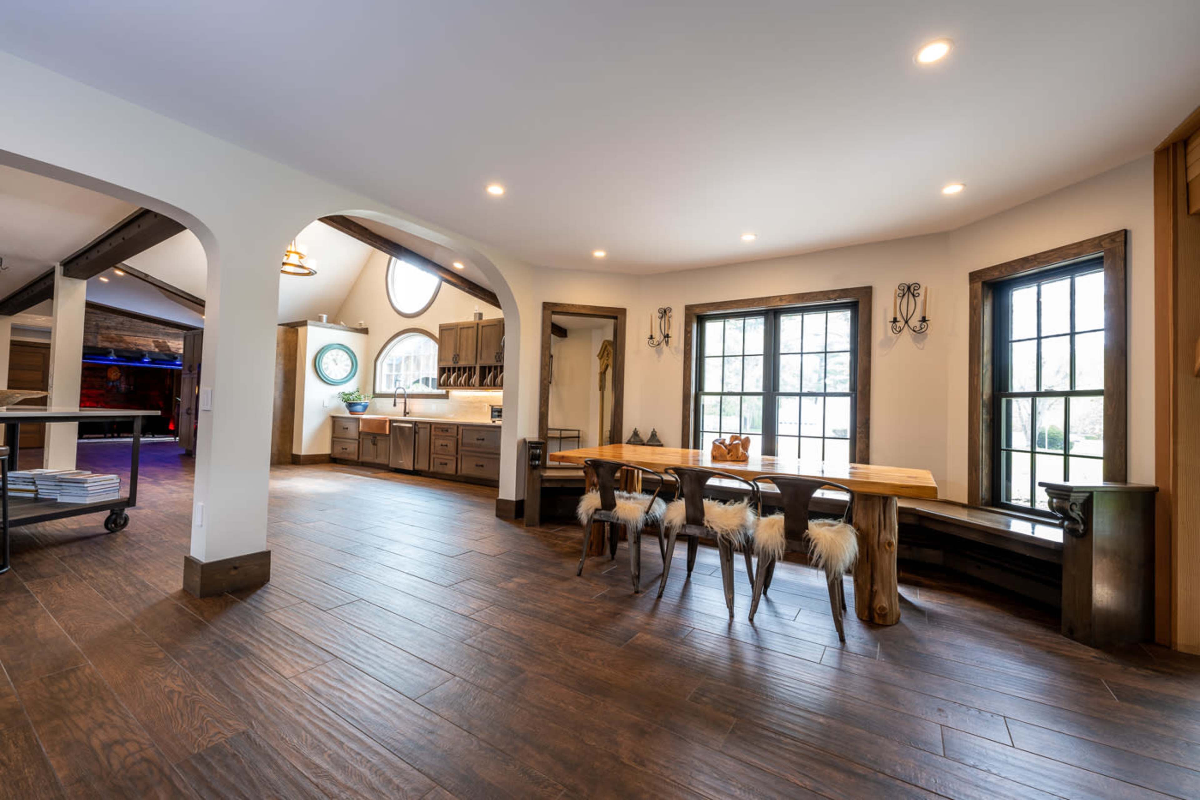 A spacious kitchen and dining area with wooden floors, large windows, and a wooden dining table surrounded by chairs.