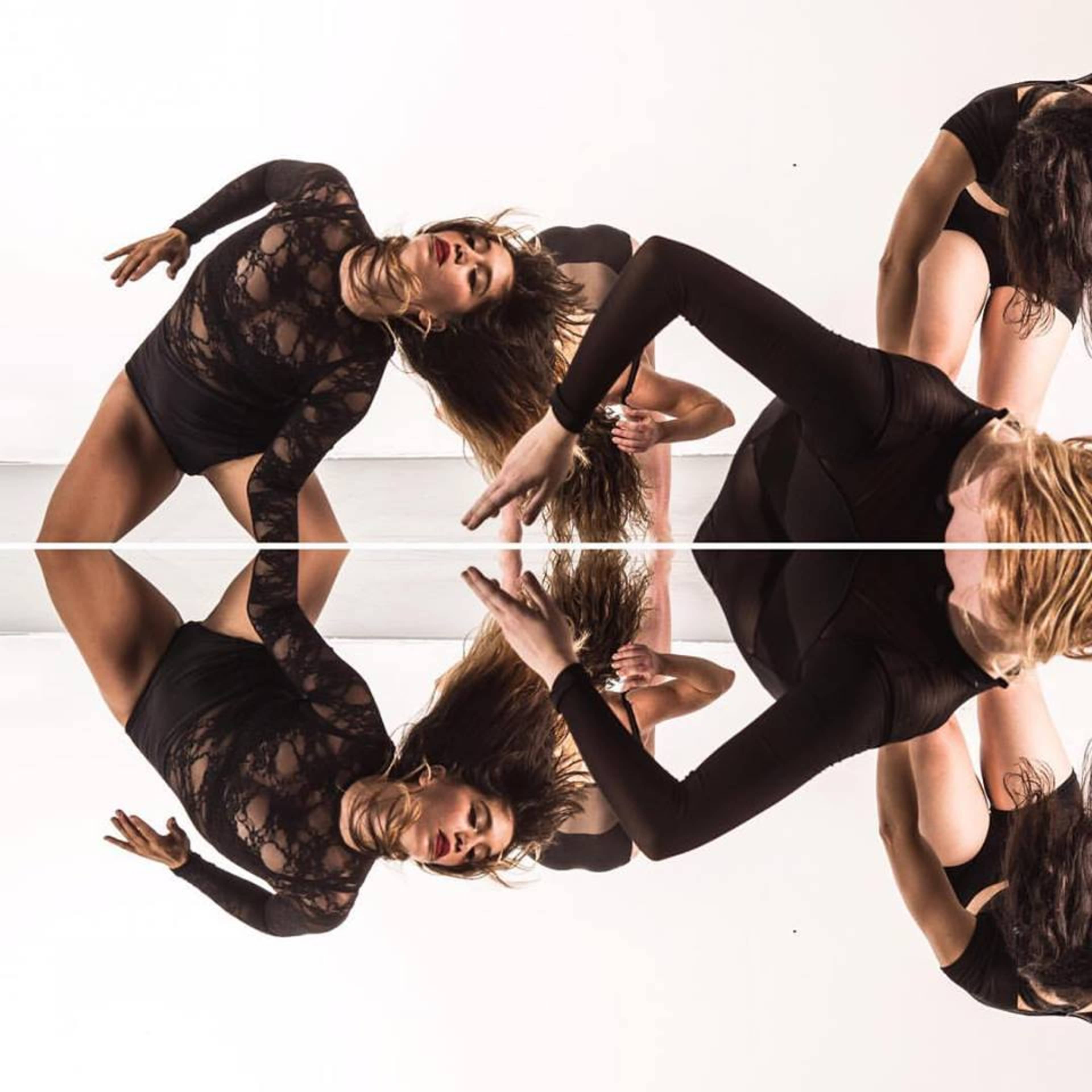 Dancers in black attire performing on a reflective surface, creating a symmetrical visual effect.