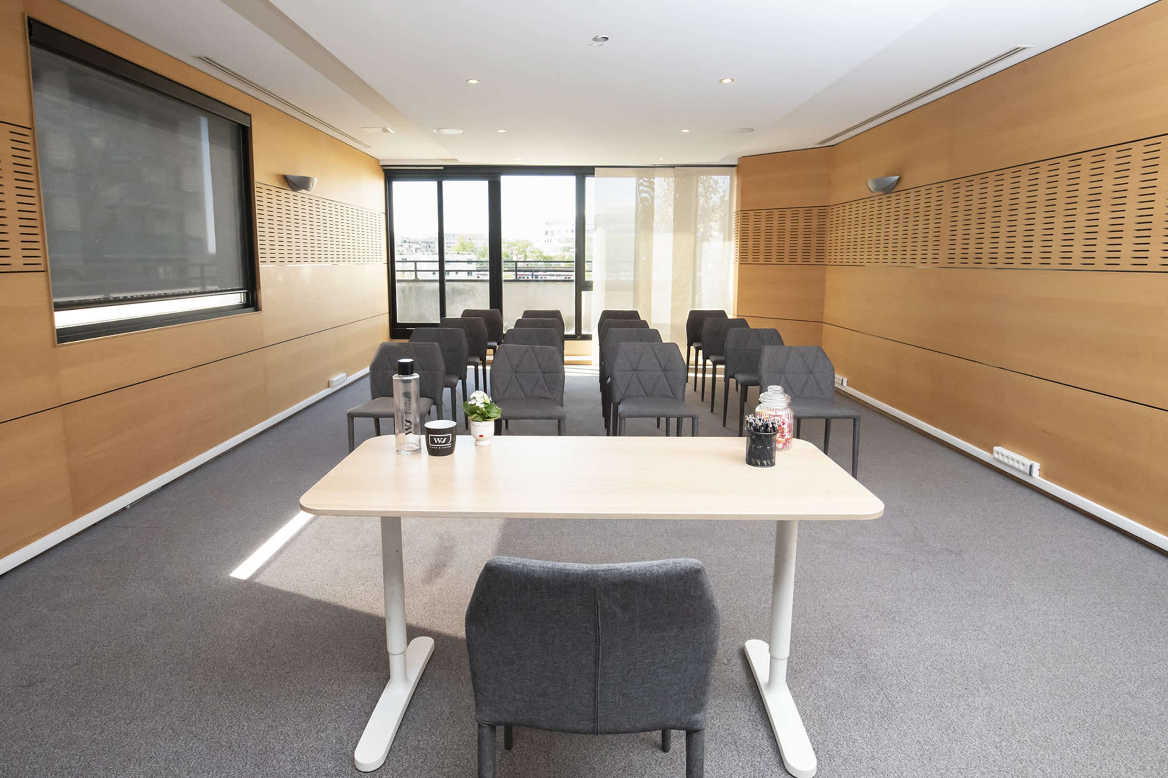 A conference room set up with rows of chairs facing a table near large windows.
