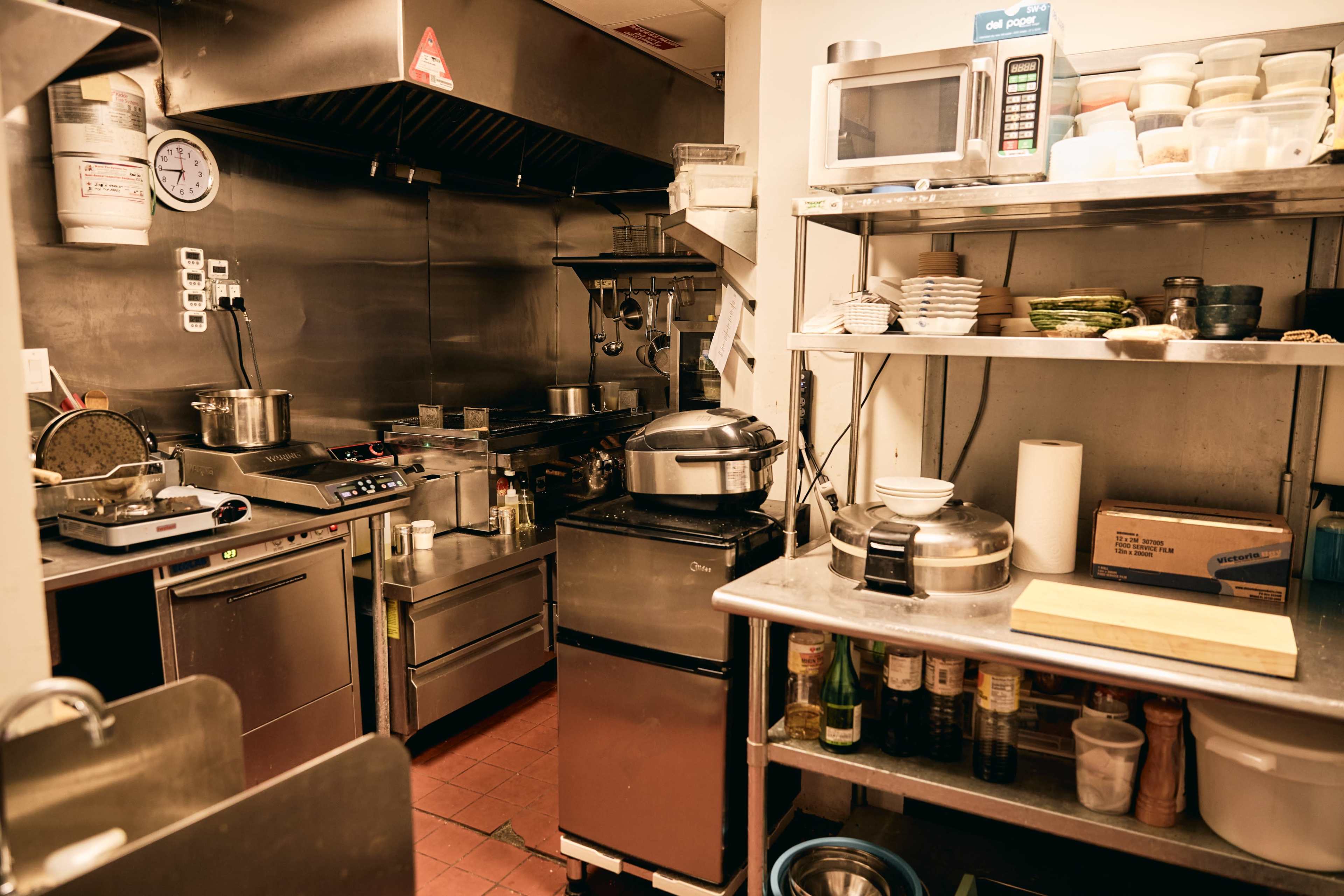 A commercial kitchen is equipped with stainless steel appliances, a microwave, and shelves holding various cooking utensils and ingredients.