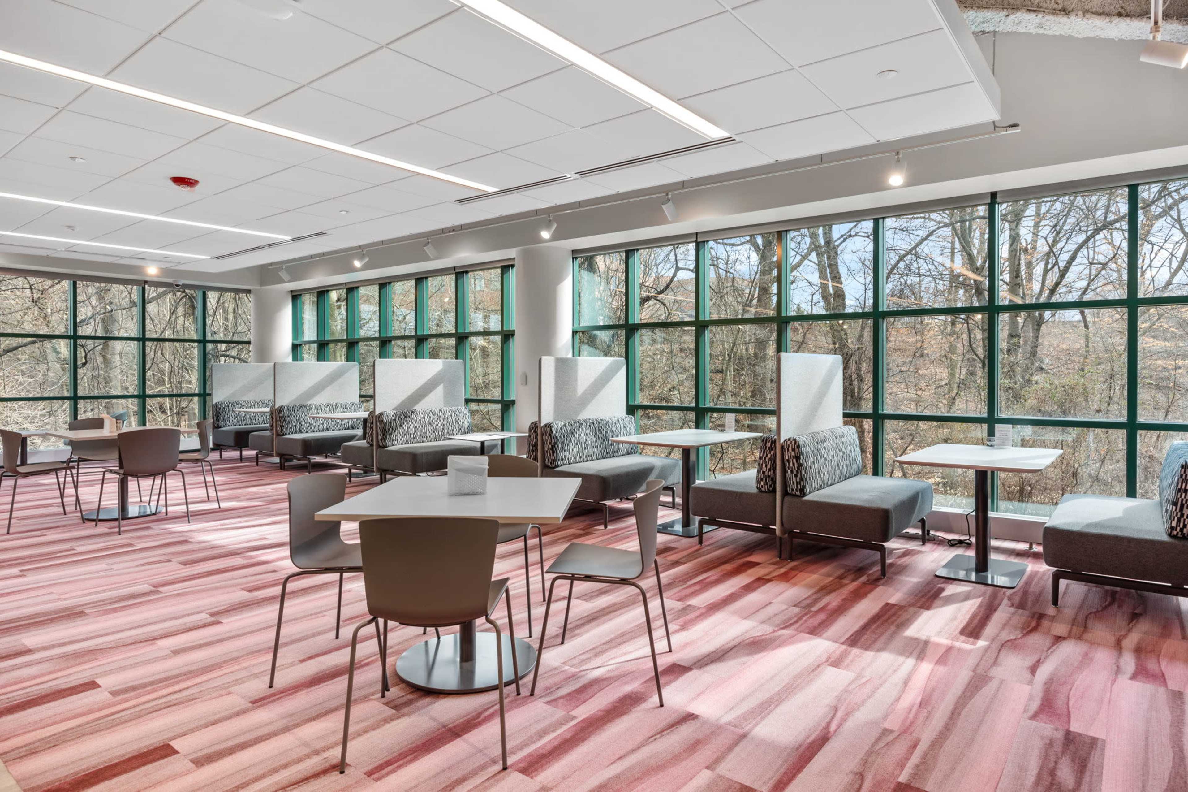 A modern, well-lit interior space with seating areas and large windows overlooking trees.