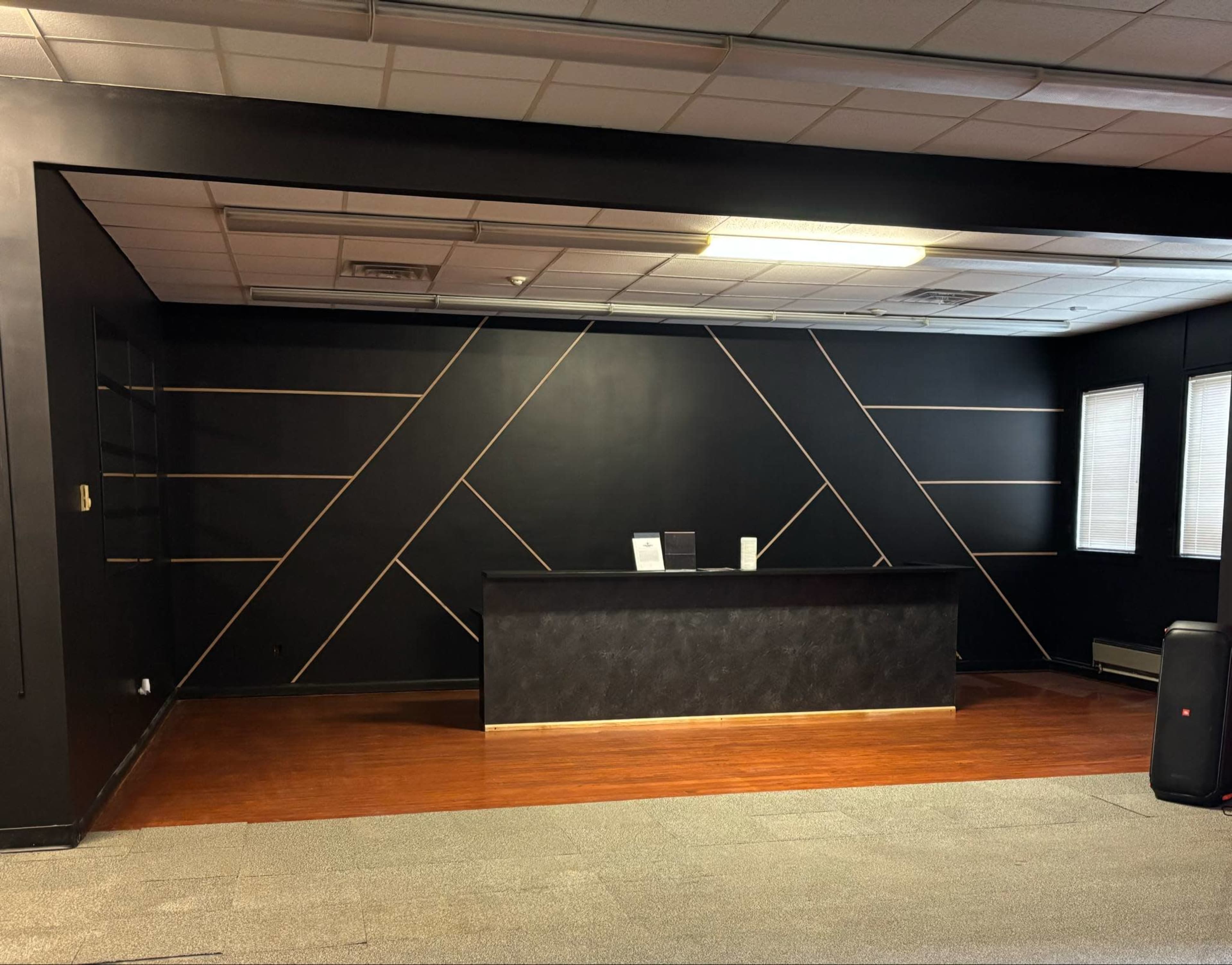 The image shows a modern office reception area with a geometric black wall design and a dark counter.