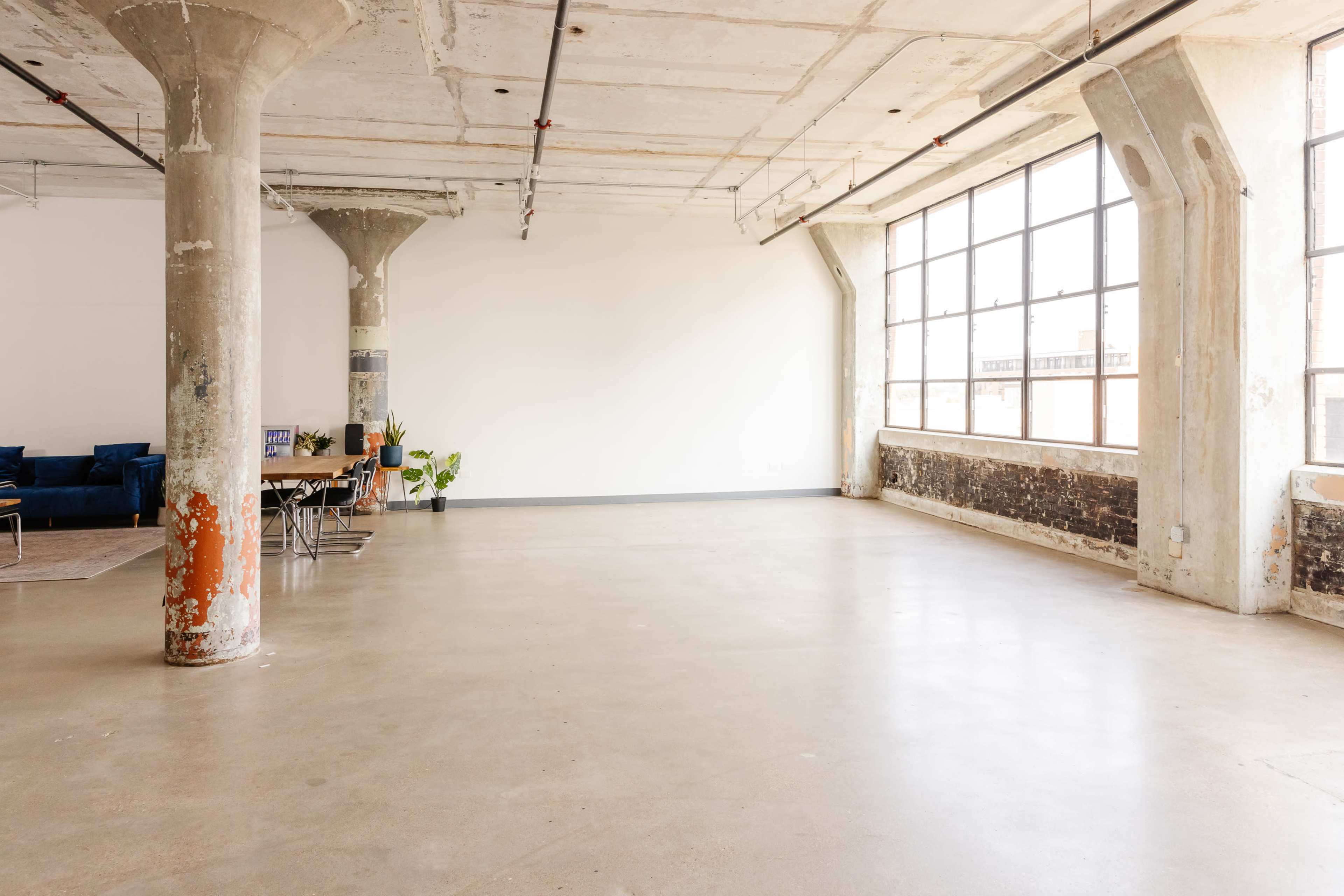 A spacious, industrial-style room with large windows, concrete pillars, and an empty floor.