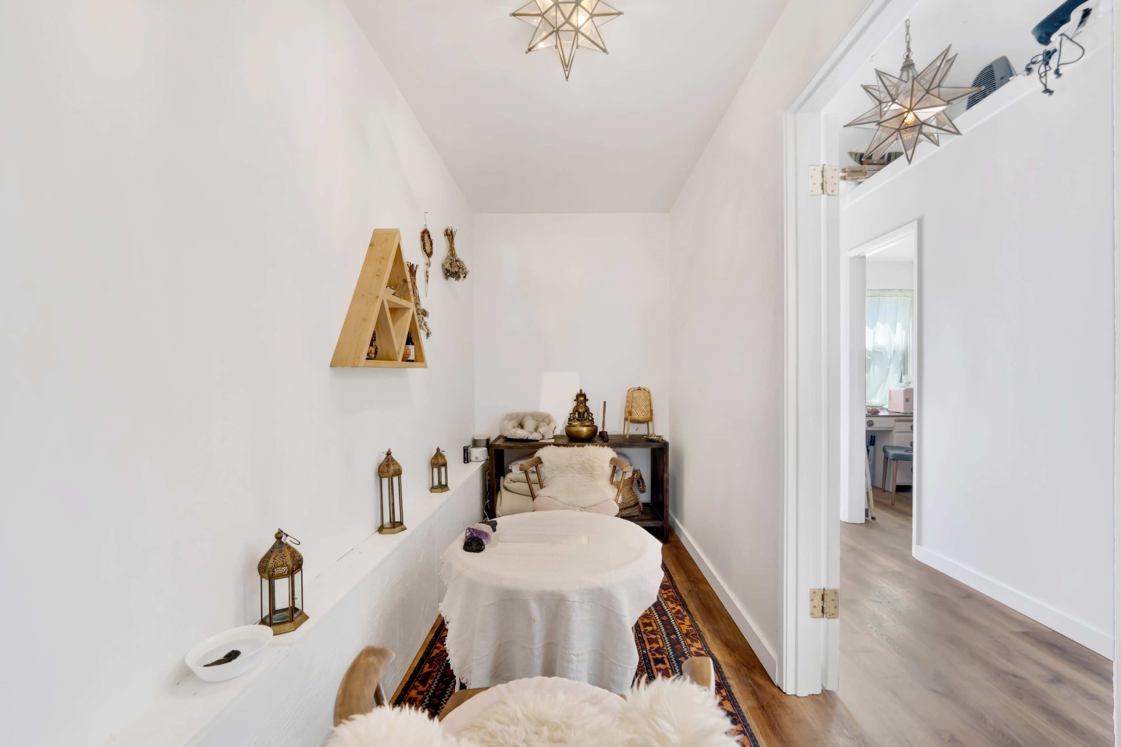 The image shows a narrow hallway with a white wall, decorated with lanterns and a wooden shelf, leading to another room.