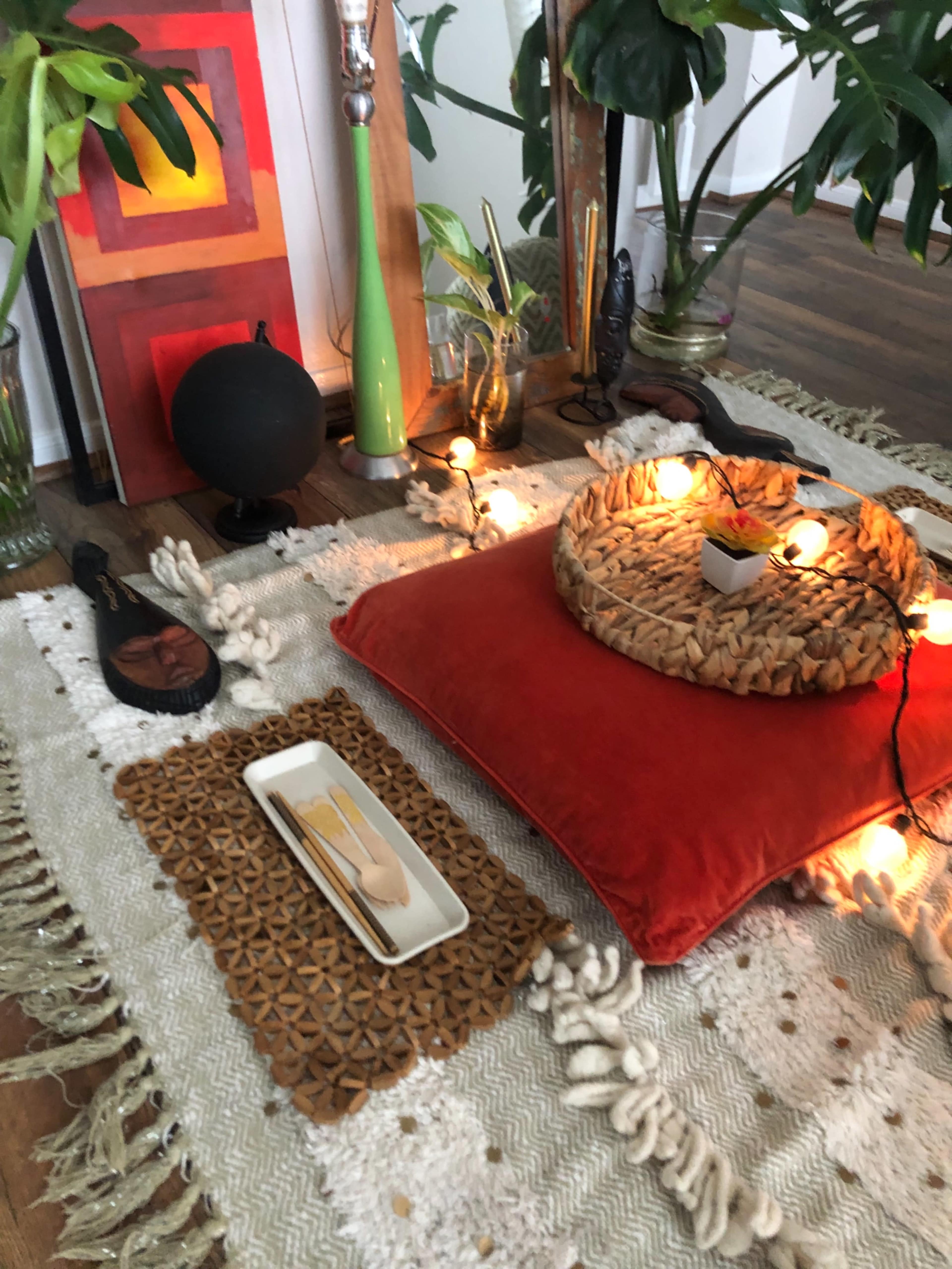 A cozy indoor setting featuring a circular woven tray, a red cushion, decorative lighting, and various objects on a textured rug.
