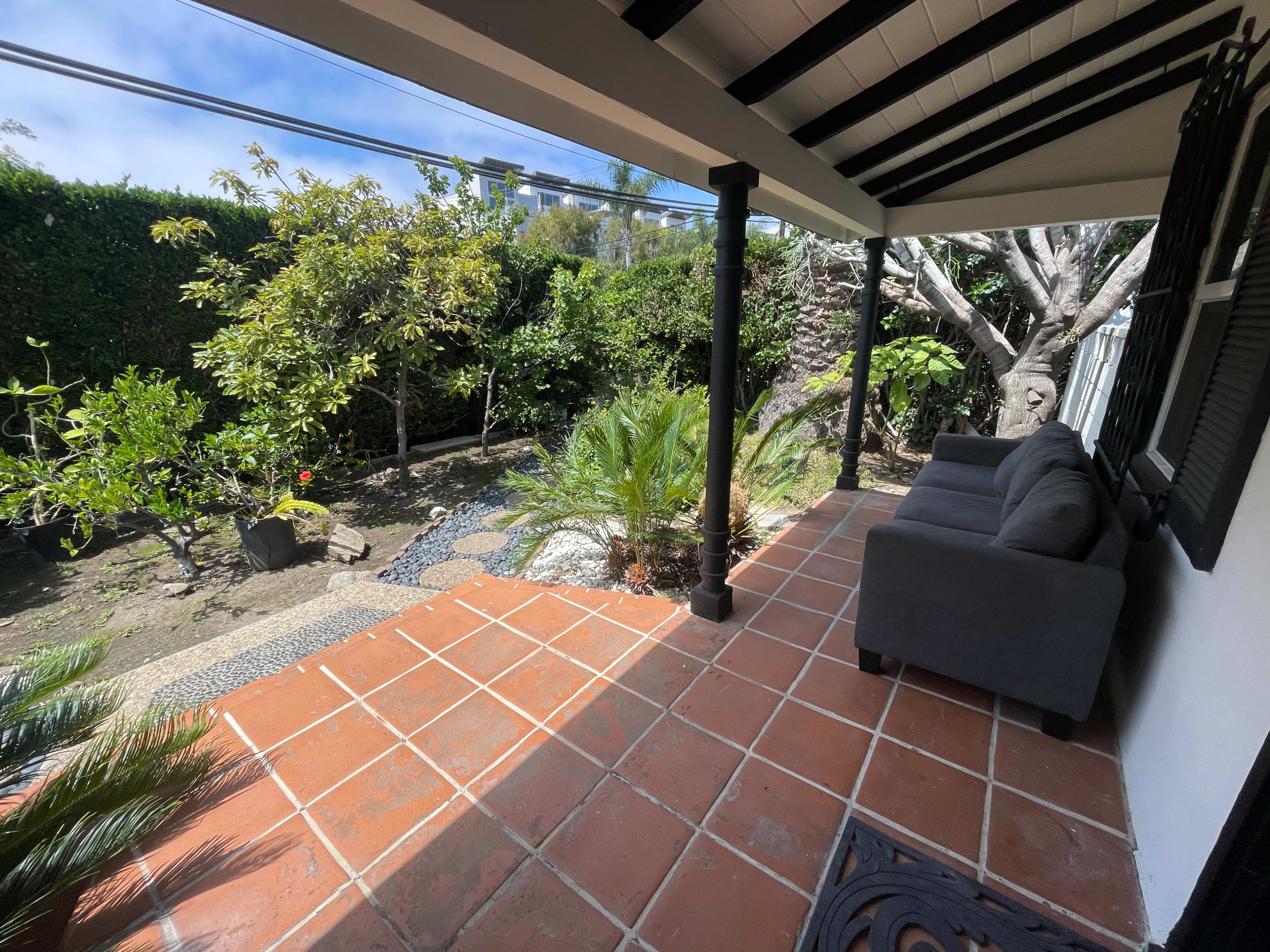 A patio with a gray sofa overlooks a landscaped garden featuring various plants and stone pathways.