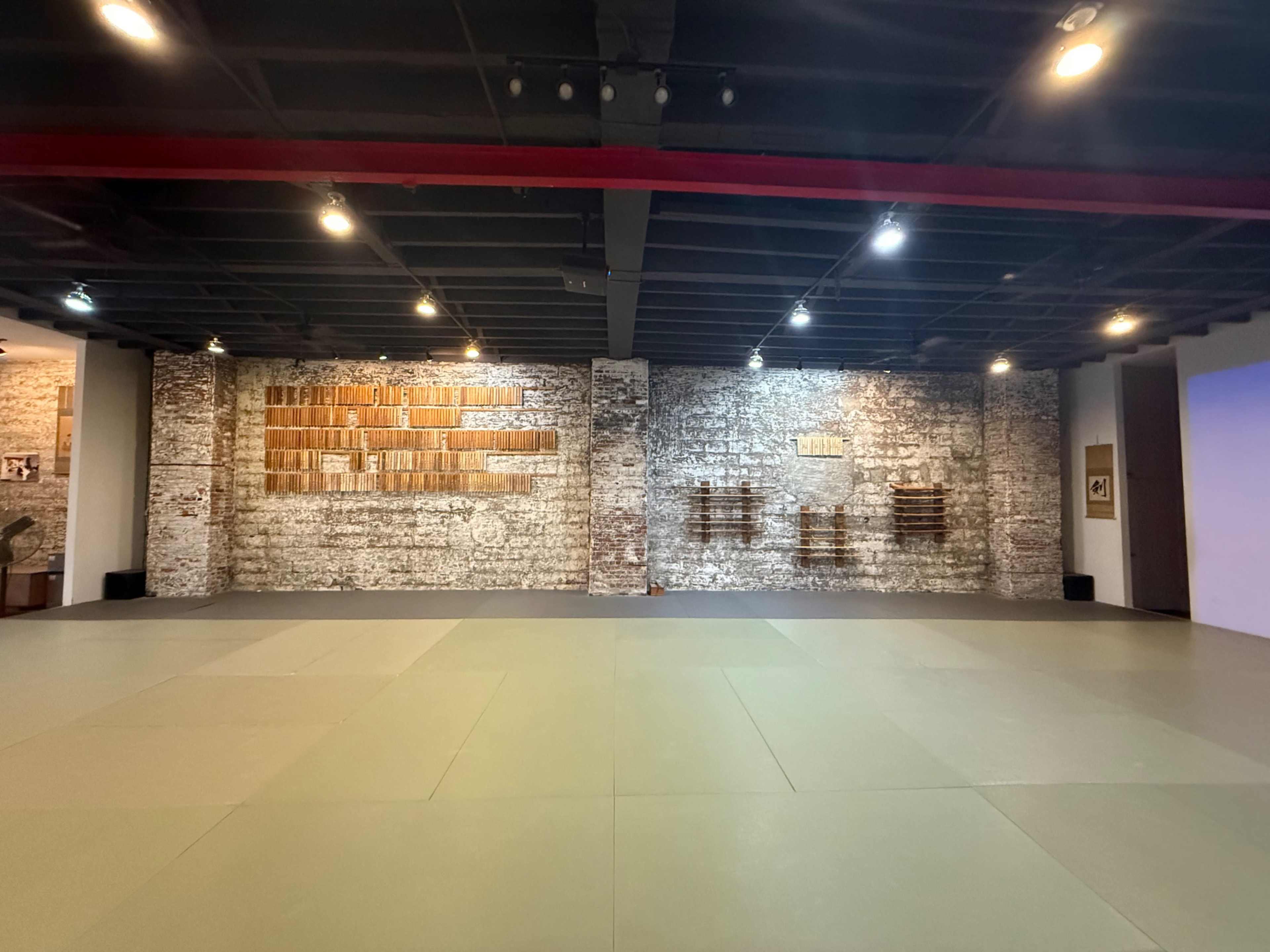 A spacious interior features a padded mat area with exposed brick walls displaying wooden panels.