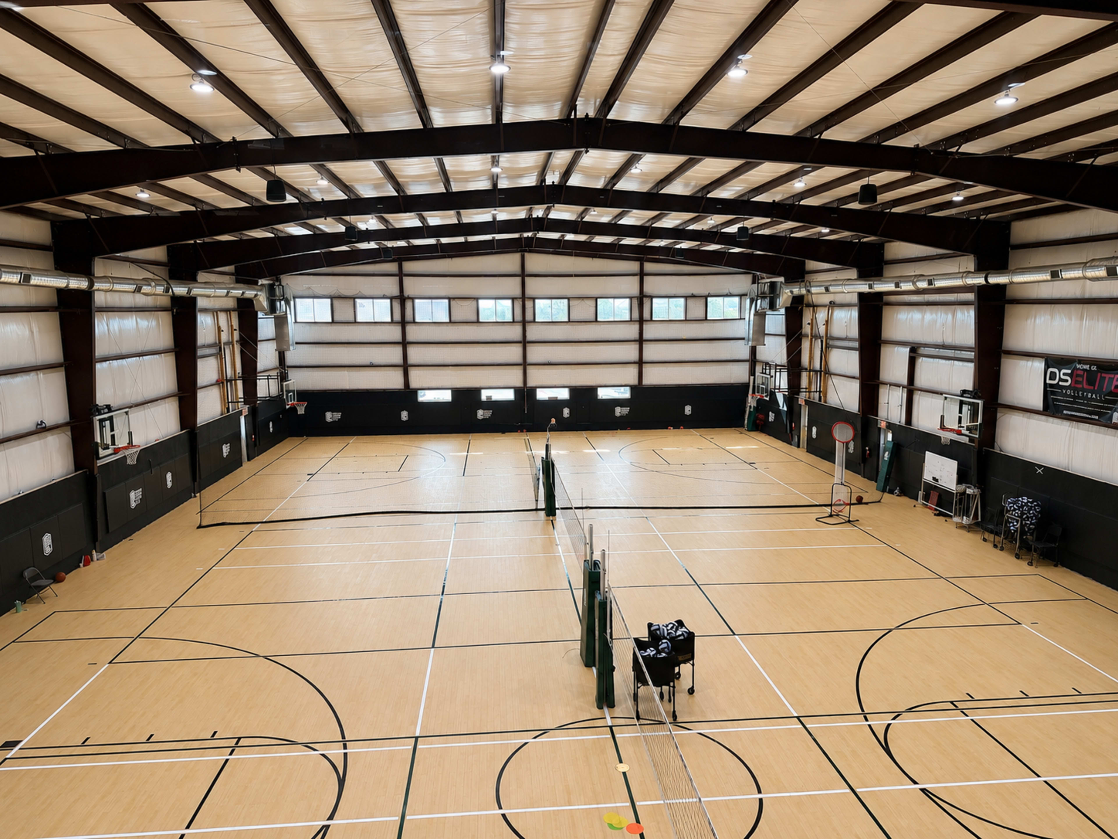 The image shows an indoor sports facility with multiple basketball courts, complete with hoops and a volleyball net.