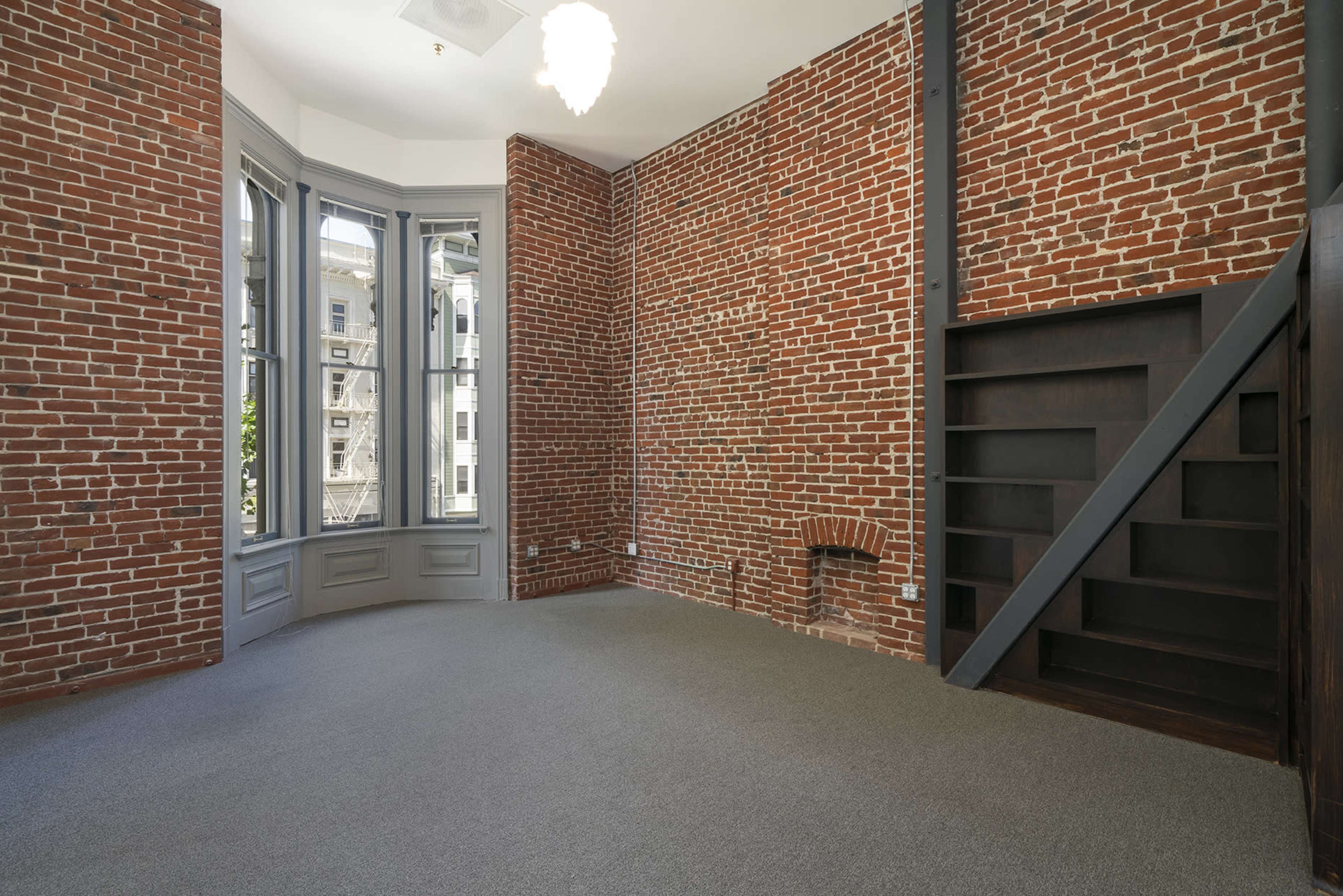A room featuring exposed brick walls, a bay window, and a staircase leading to a loft area.