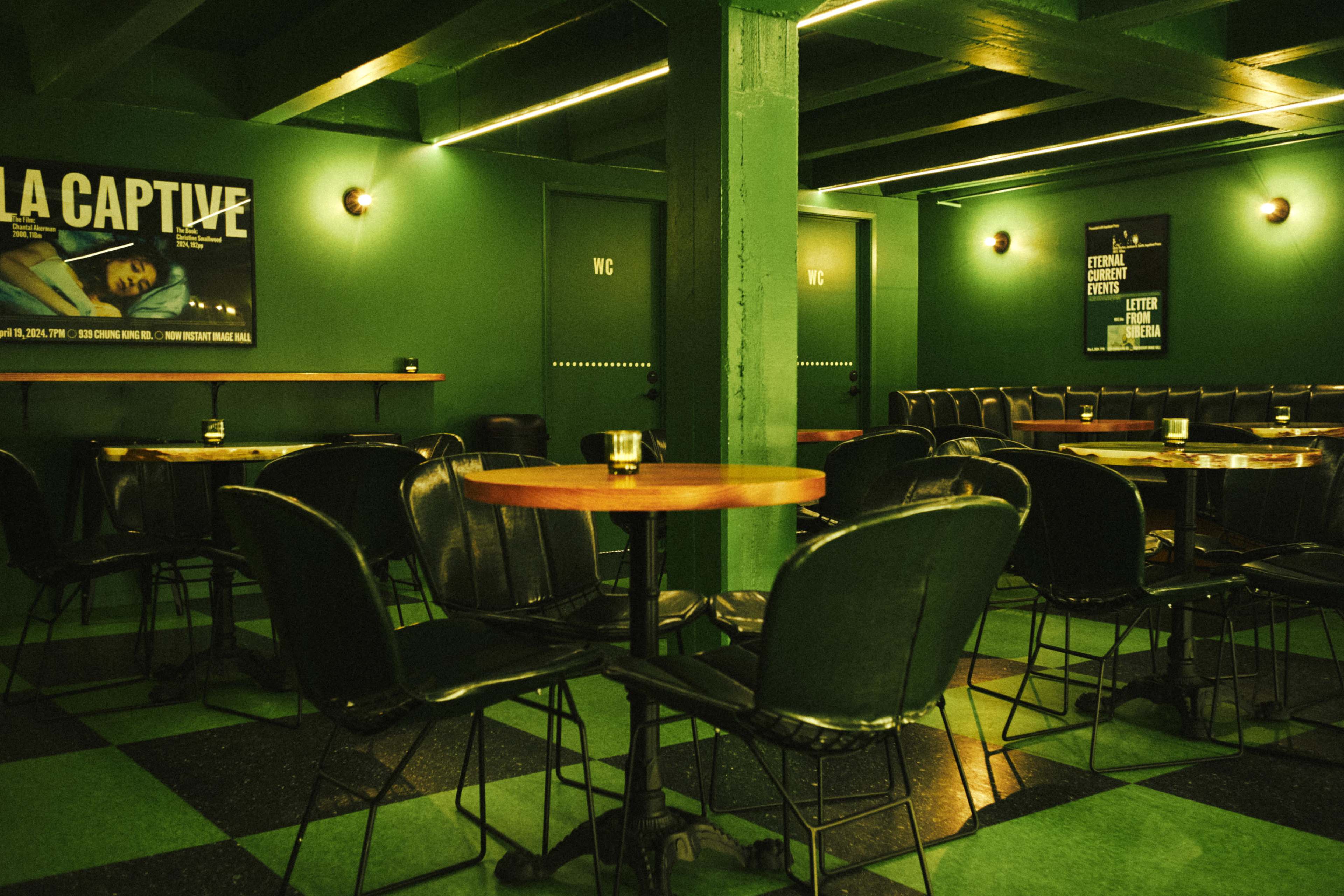 The image shows an empty café with green walls, round tables, and black chairs, illuminated by soft lighting.