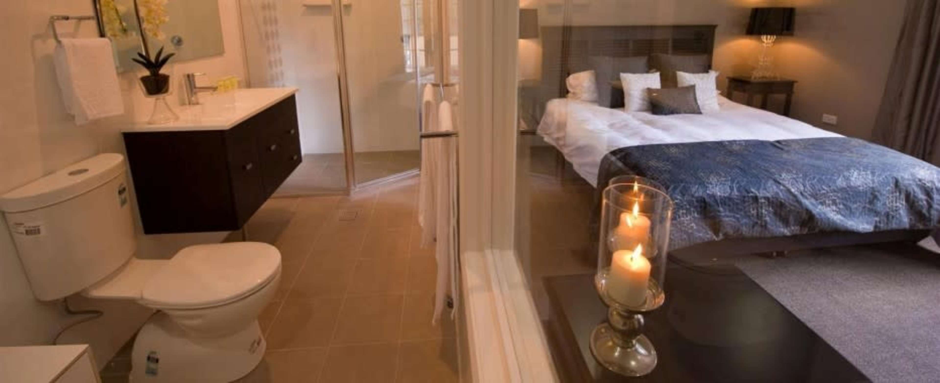 A modern bathroom with a toilet and sink adjacent to a bedroom featuring a large bed with decorative pillows.