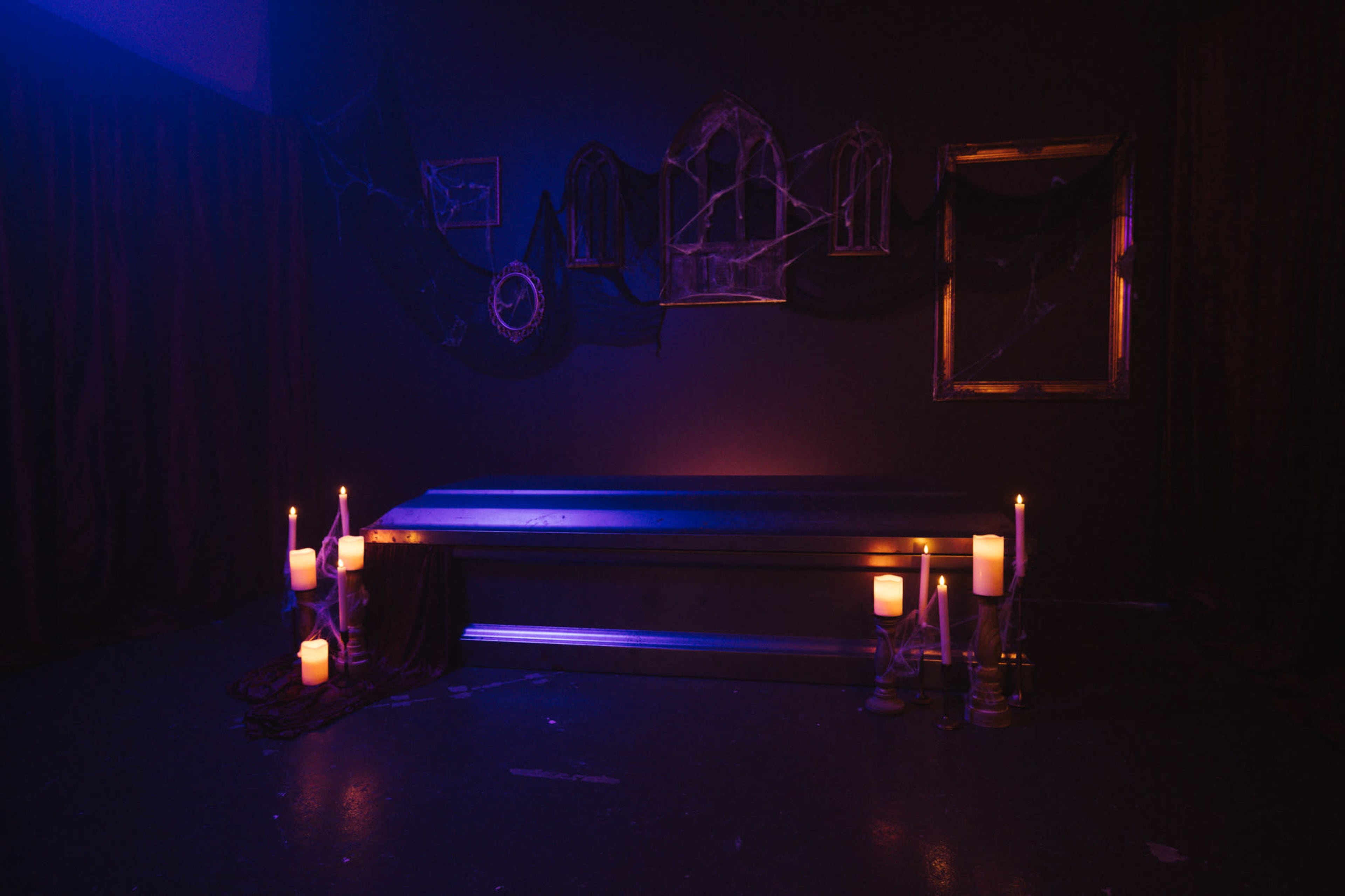 The image shows a dimly lit room with a metallic table surrounded by candles and cobwebs, along with mirrors mounted on the wall.