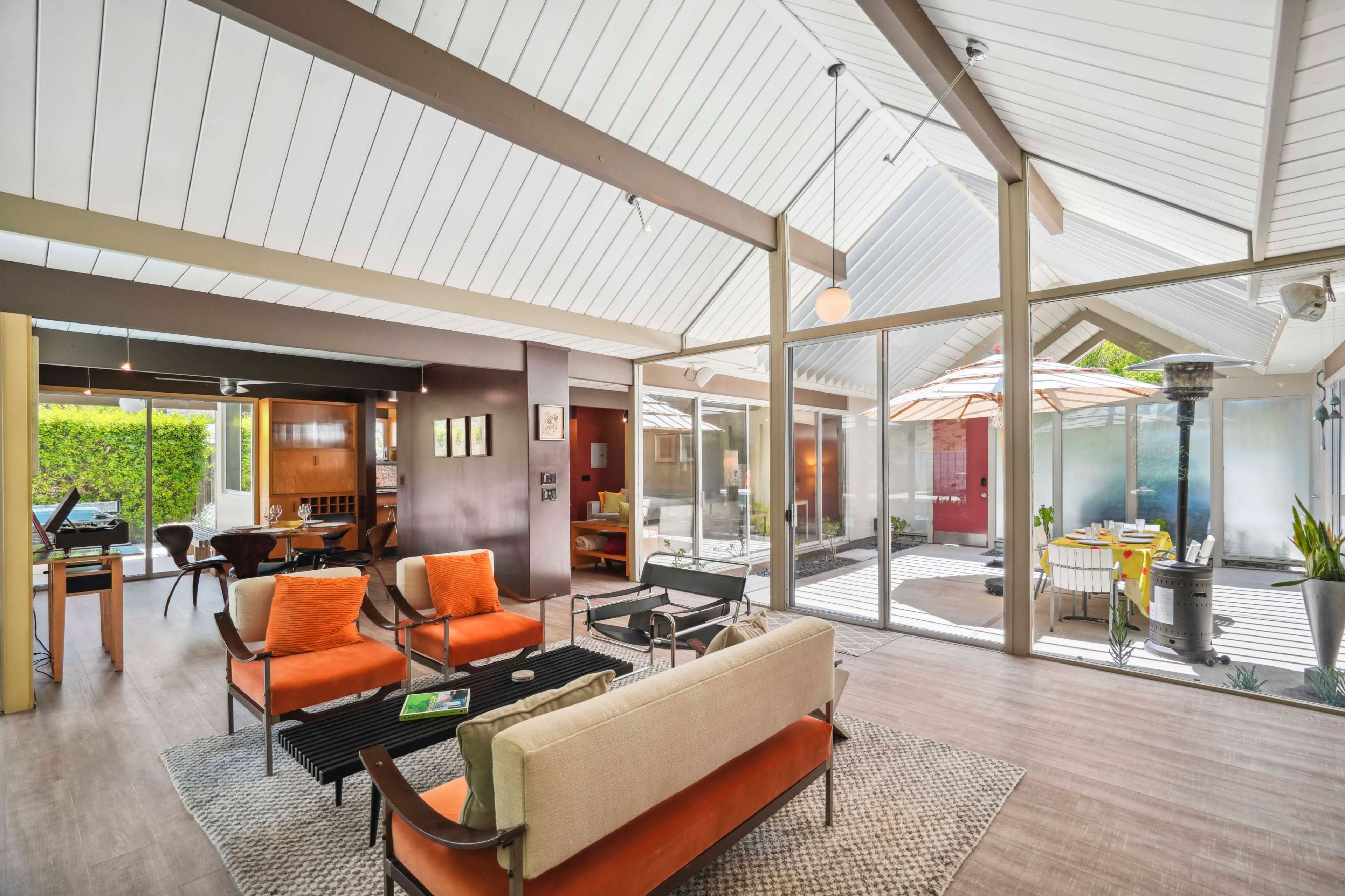 A modern indoor living space featuring a mix of seating arrangements, large glass windows, and a view of an enclosed patio.