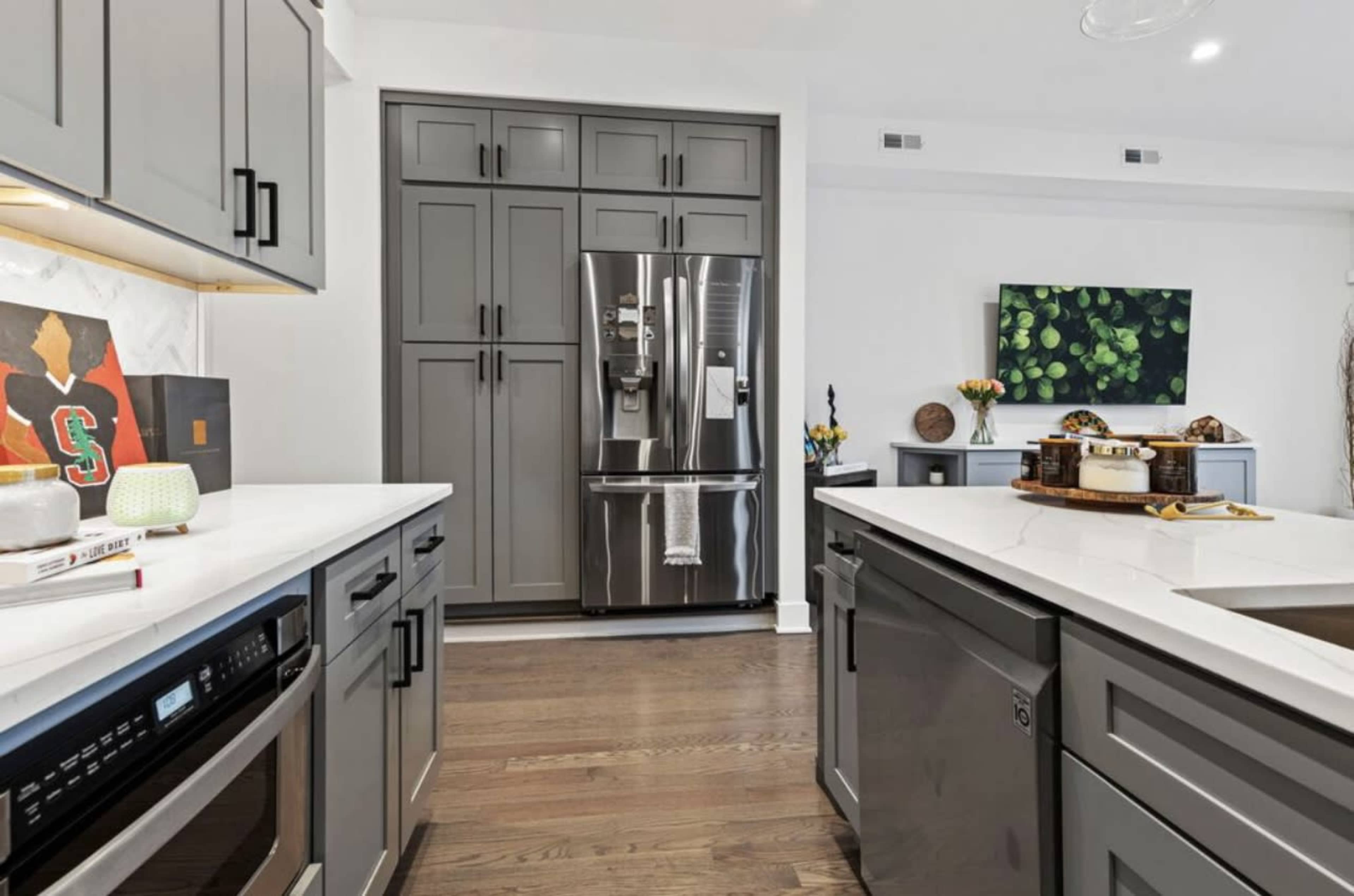 The image shows a modern kitchen with gray cabinetry, stainless steel appliances, and a wooden floor.