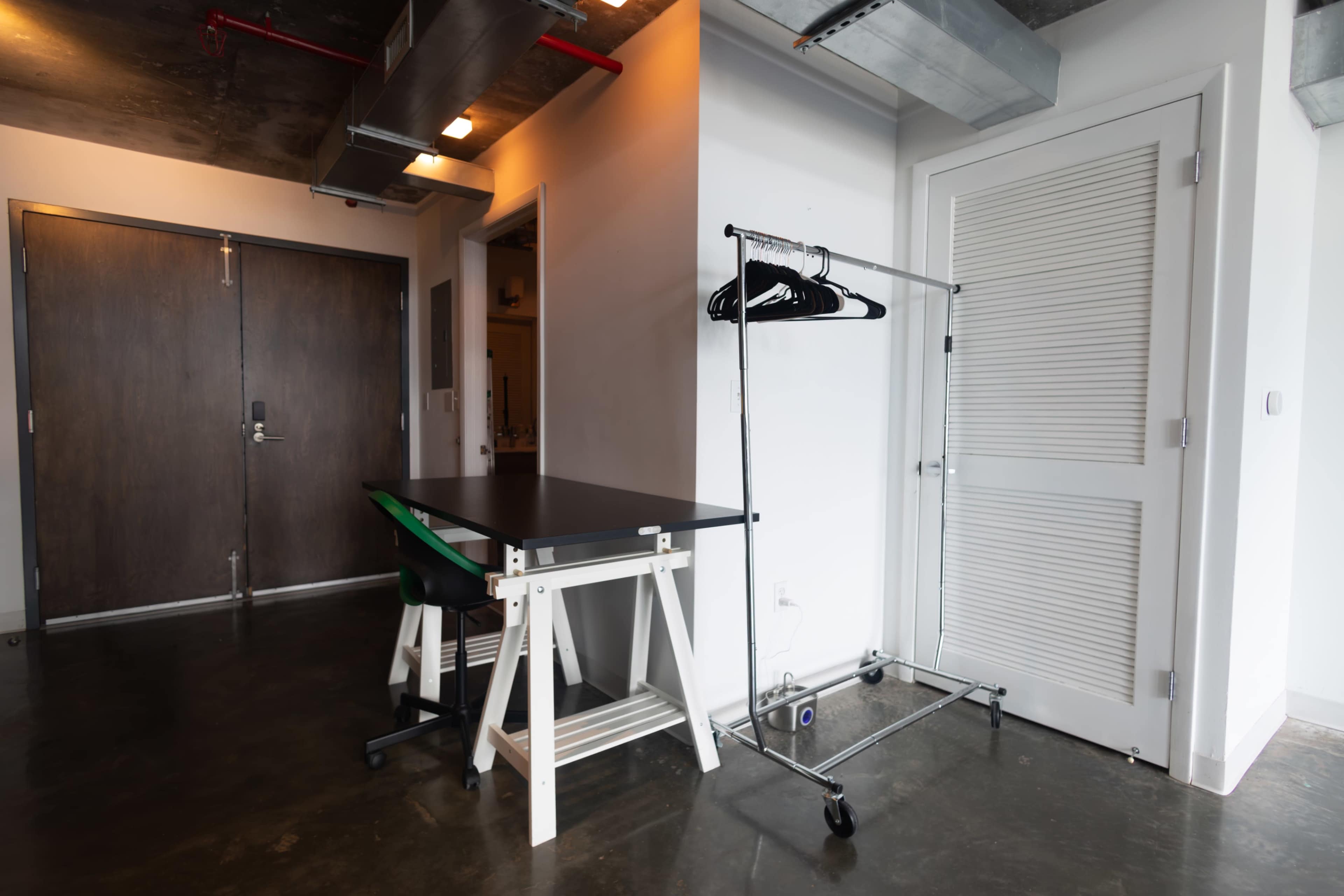 The image shows a modern entryway with a table, a clothing rack with hangers, and a door leading to another room.