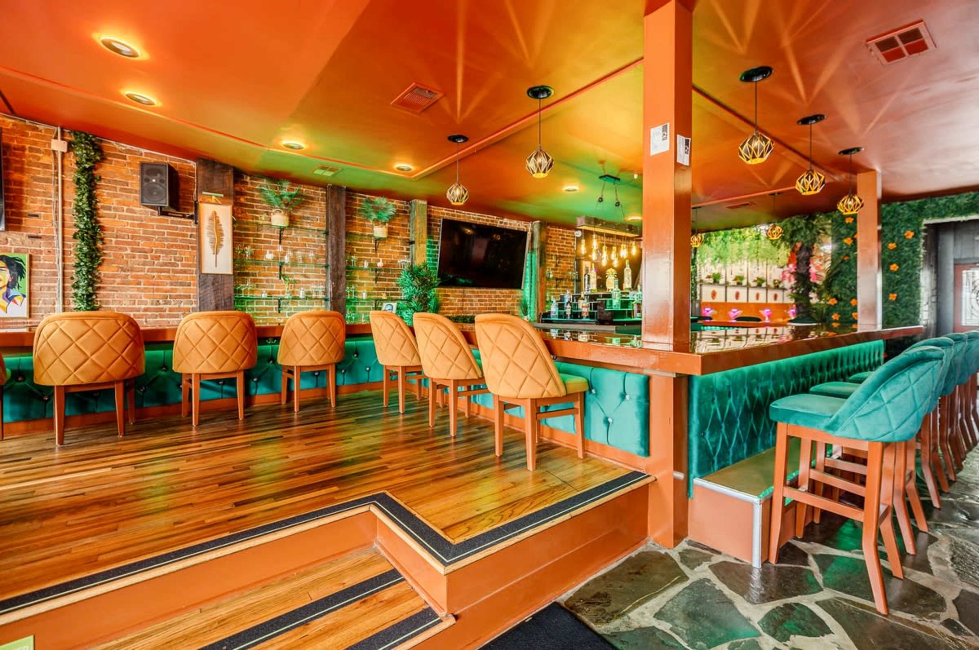 A vibrant restaurant interior featuring orange and green seating, wooden flooring, and exposed brick walls.
