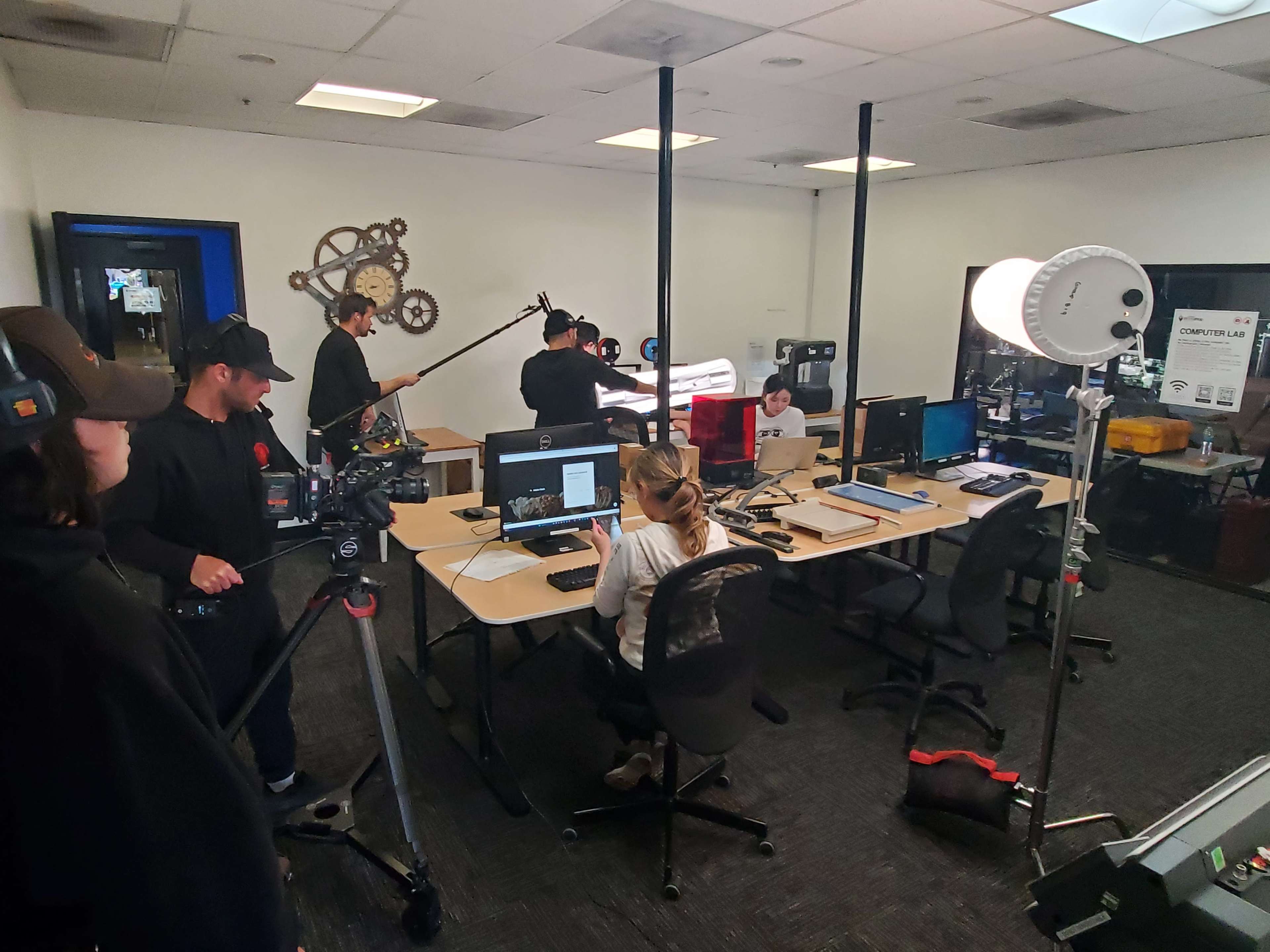 A group of people works in an office-like space equipped with multiple computers and filming equipment.