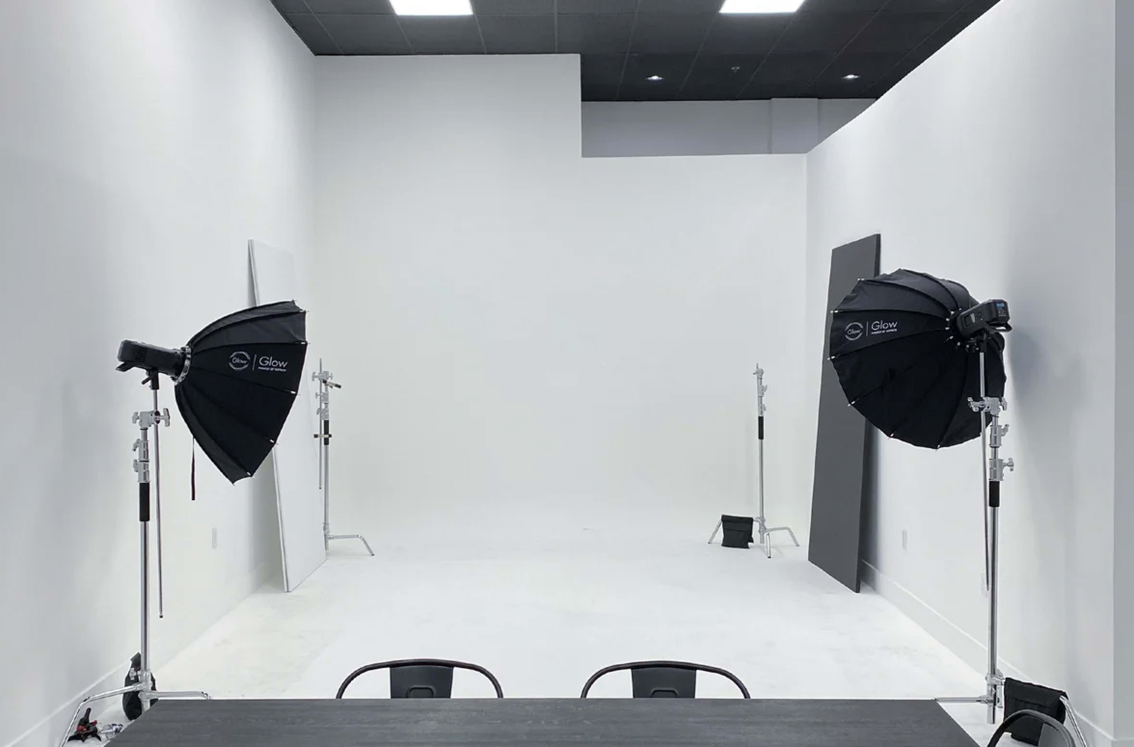 A minimalist studio space with white walls, a light gray floor, and two black softbox lights positioned on either side.