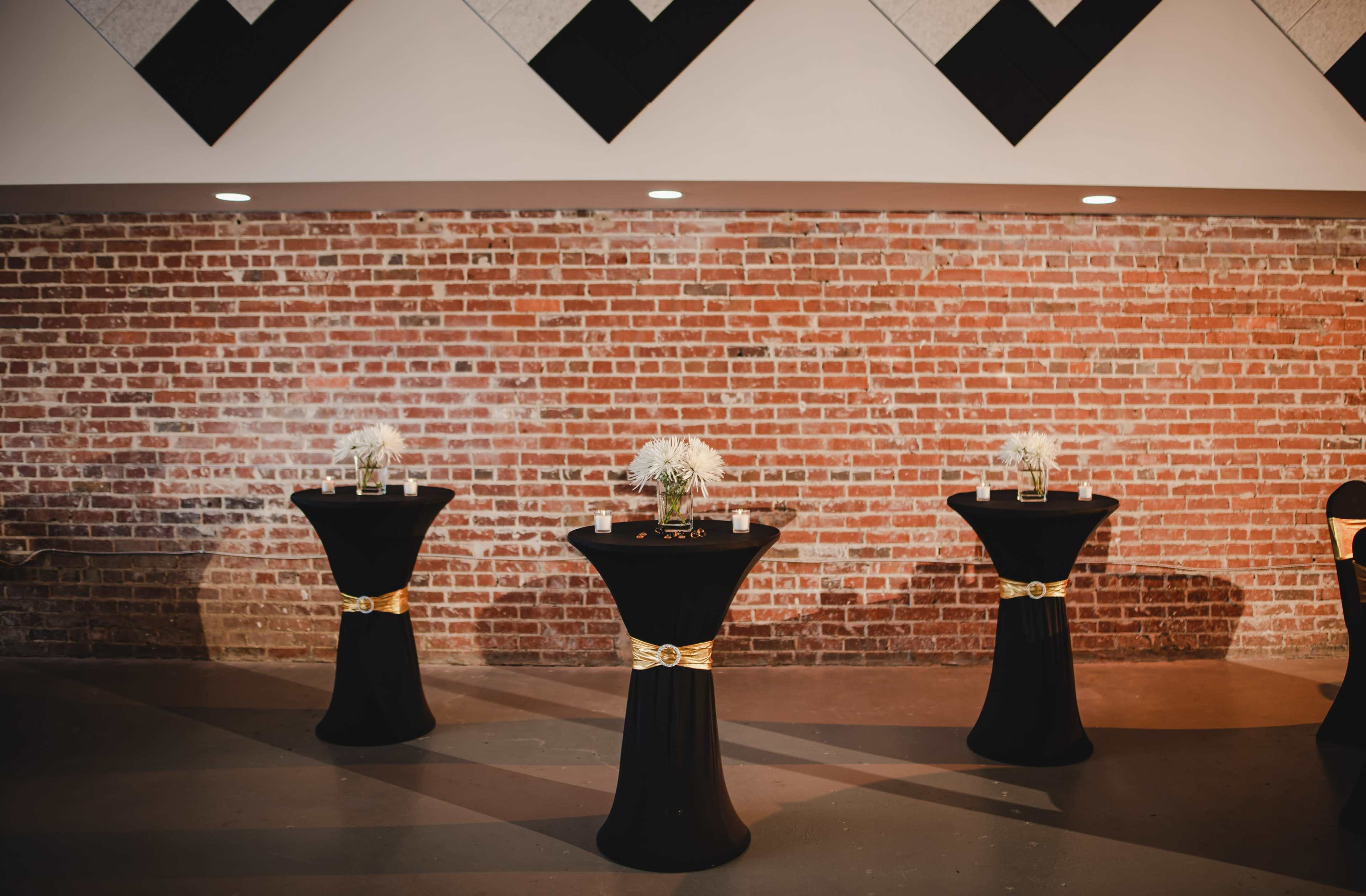 Three black-topped tables with gold accents are arranged in front of a red brick wall.
