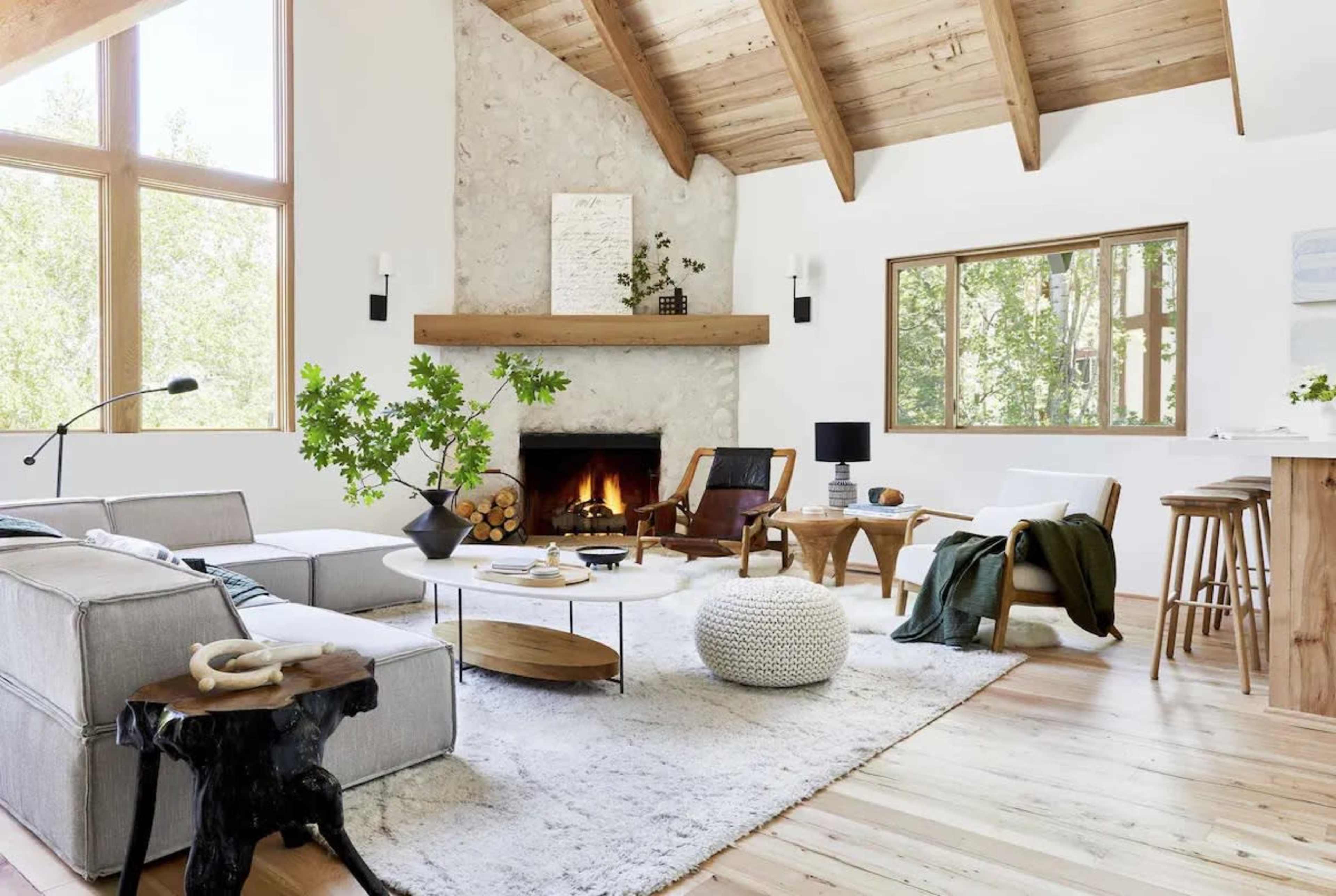 A spacious living room with a stone fireplace, large windows, and a mix of modern and rustic furniture.