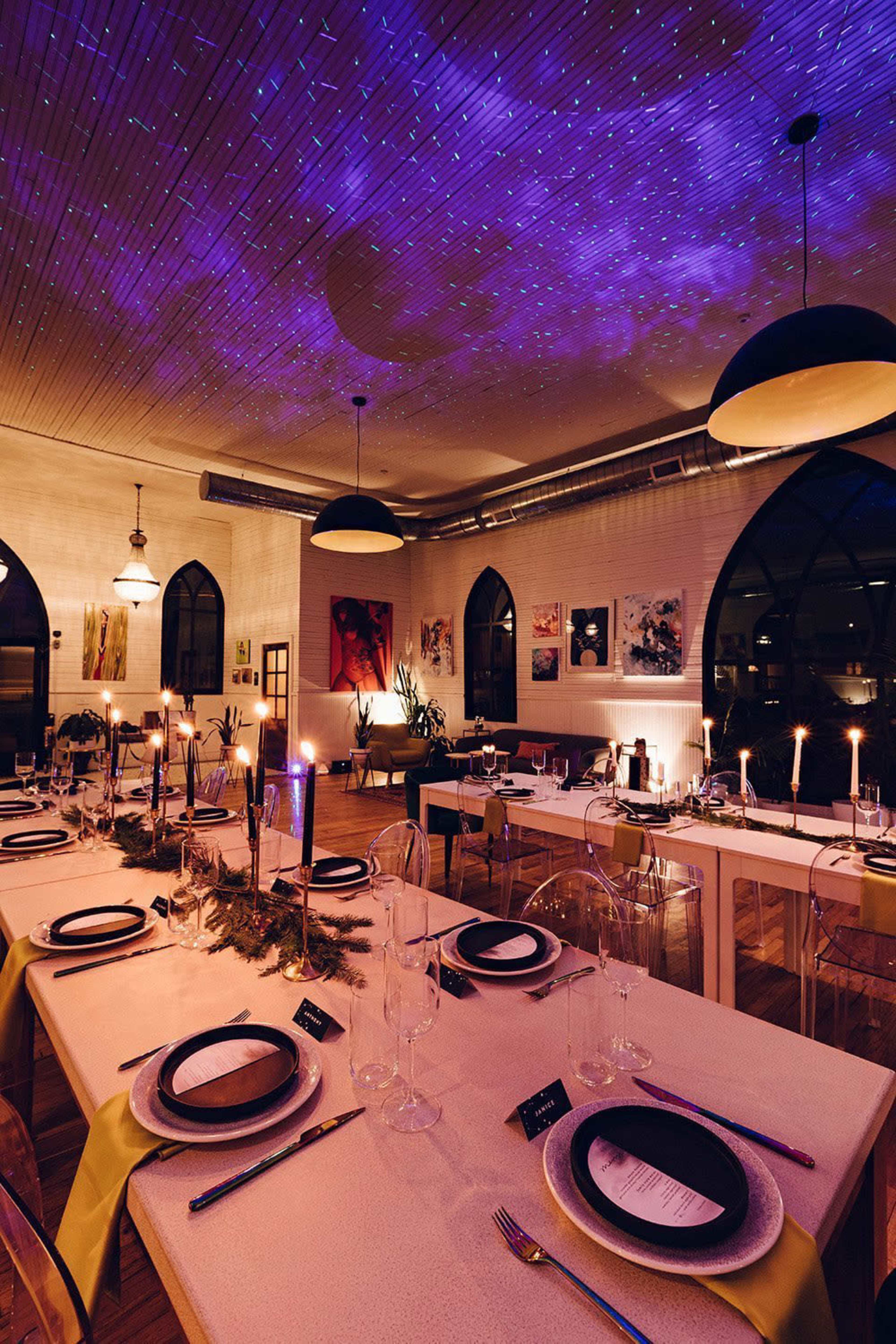 A dining room is set with tables adorned with plates and candles under a starry ceiling projection.