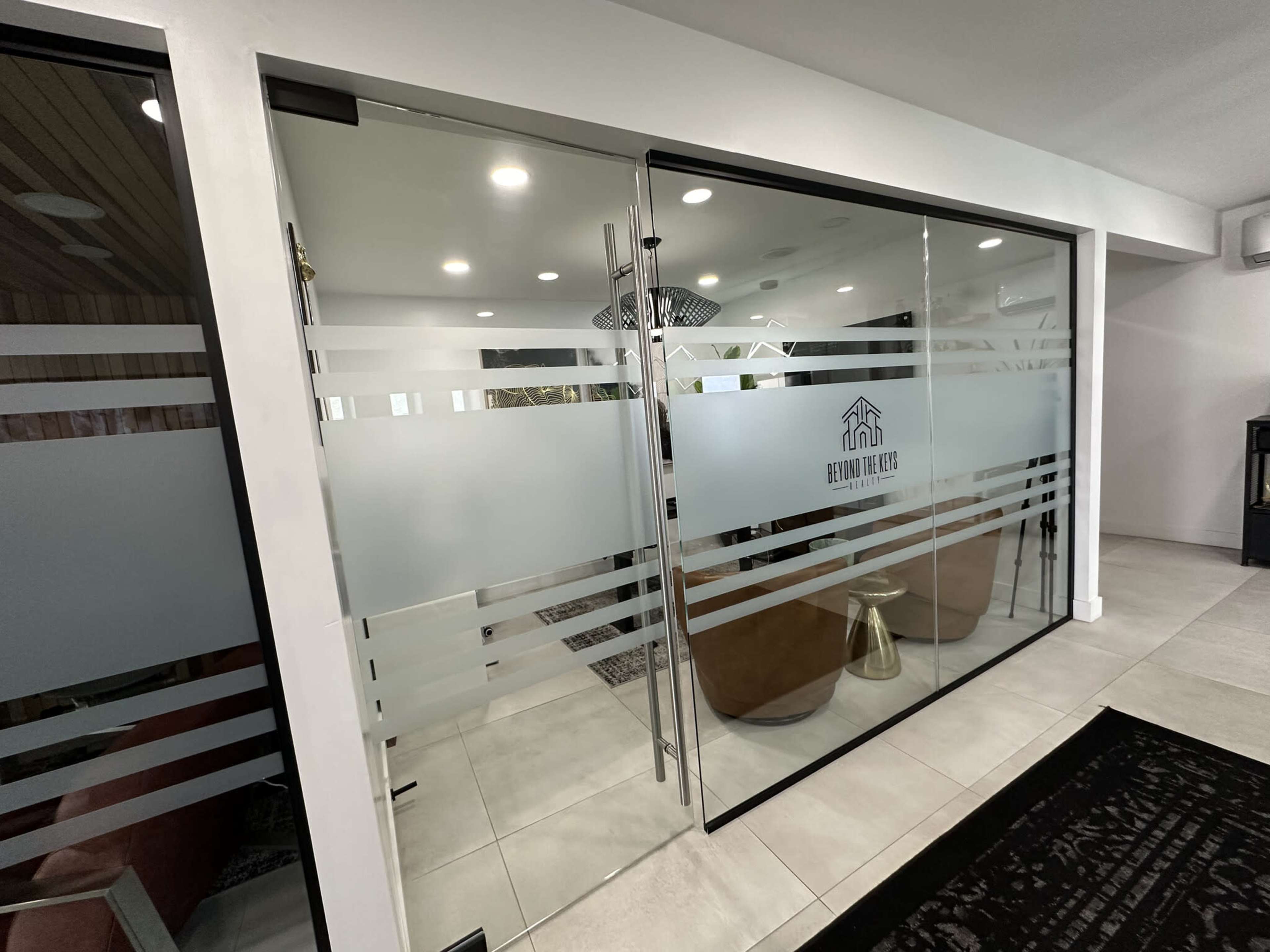 The image shows a modern office space with glass sliding doors featuring frosted patterns and an emblem.