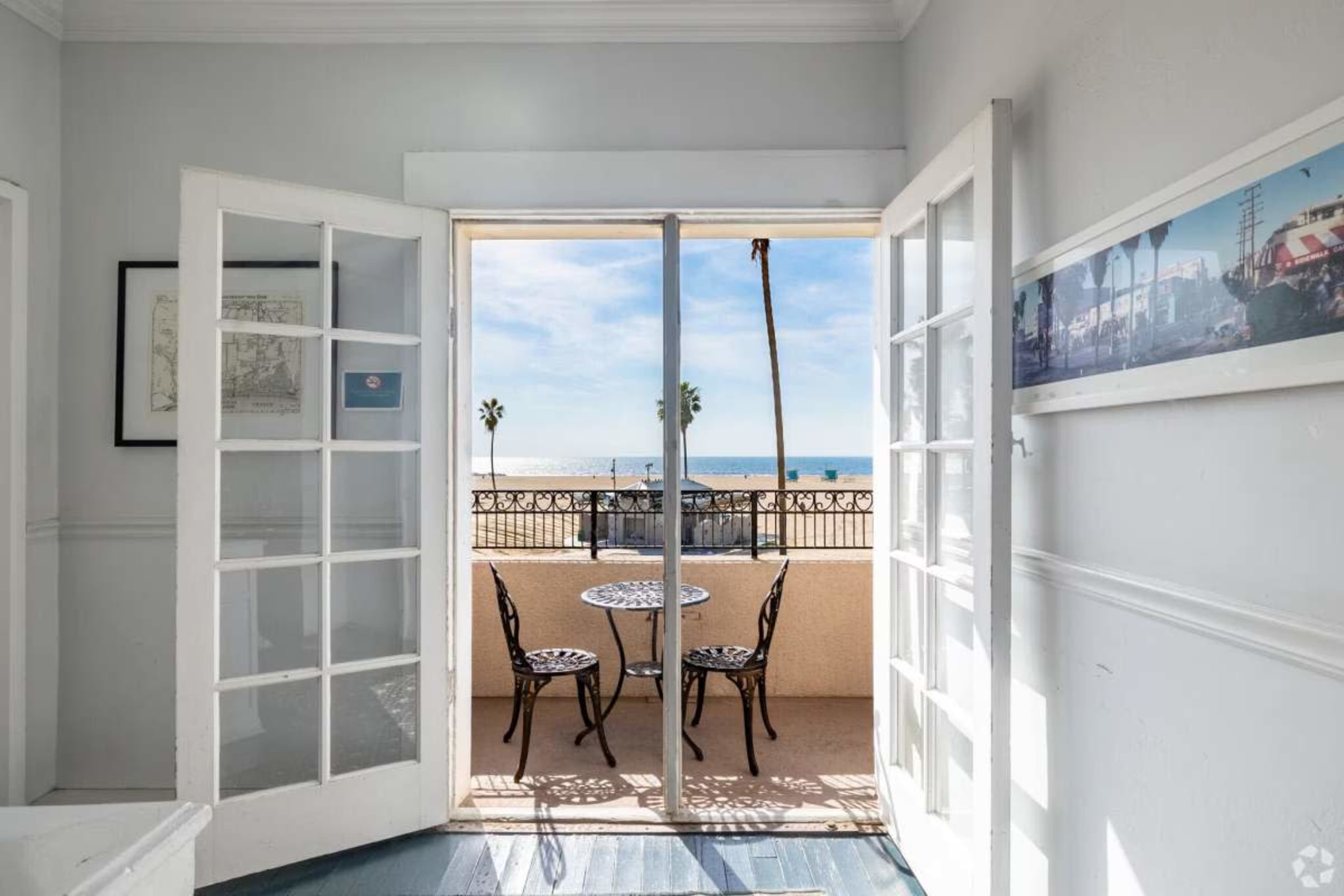 A set of open French doors leads from an indoor space to a balcony overlooking the ocean, featuring a small table and two chairs.