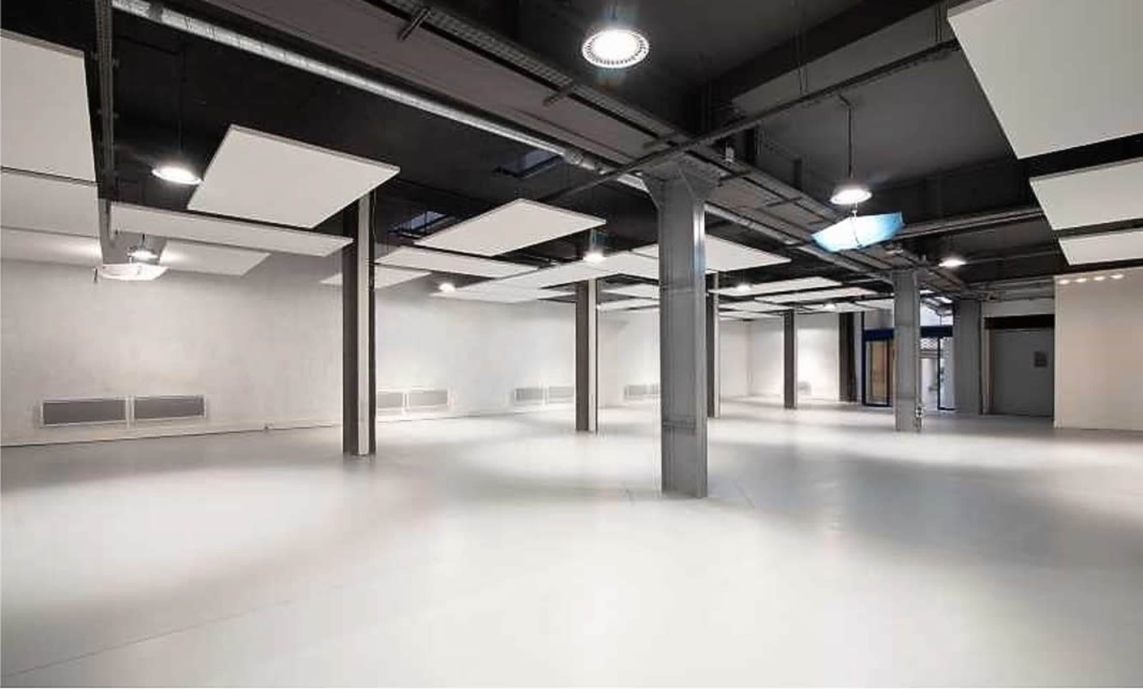 A spacious, well-lit room with a smooth white floor and exposed structural beams.