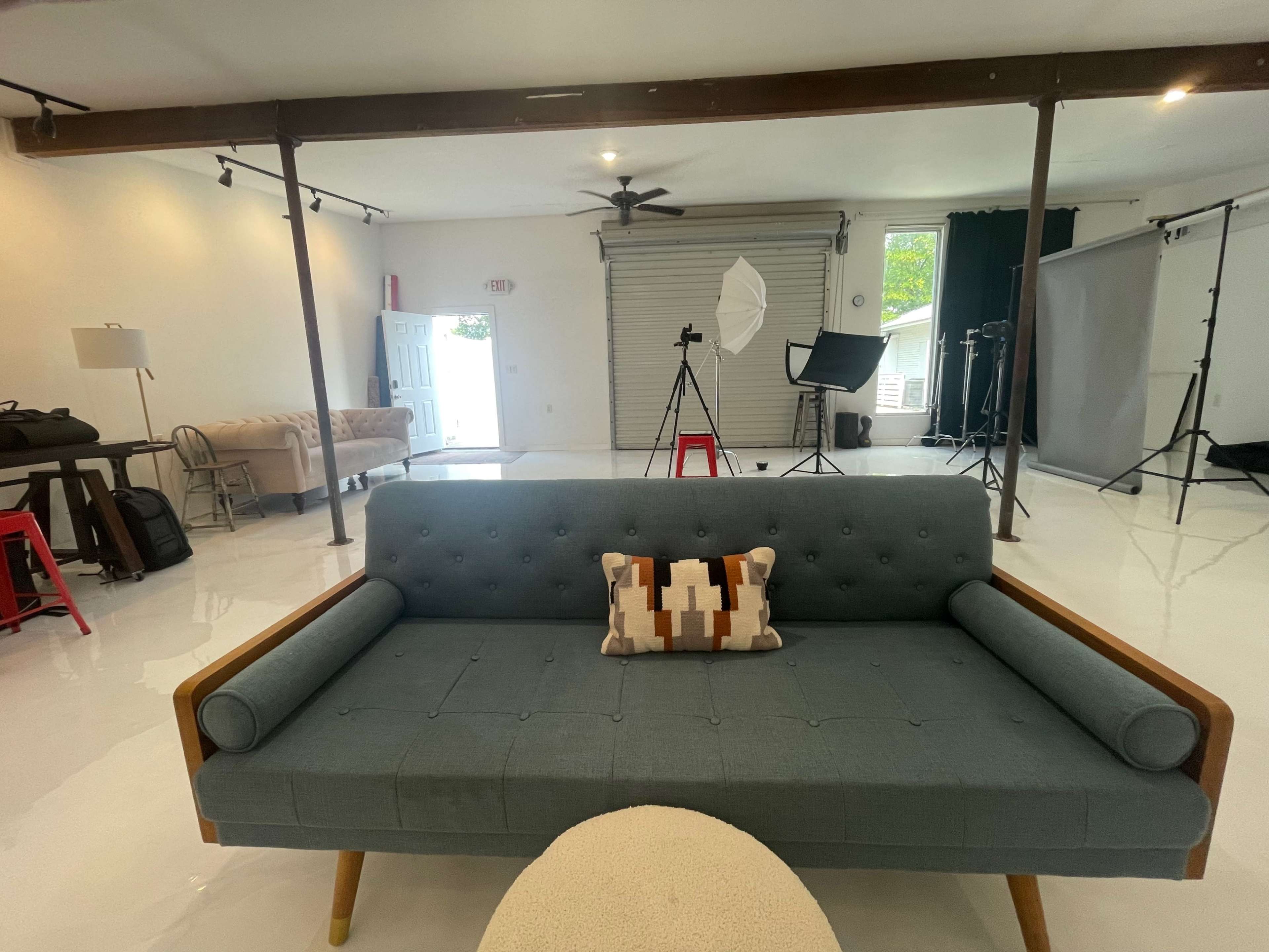 A spacious studio with a blue sofa, photography equipment, and bright white flooring.